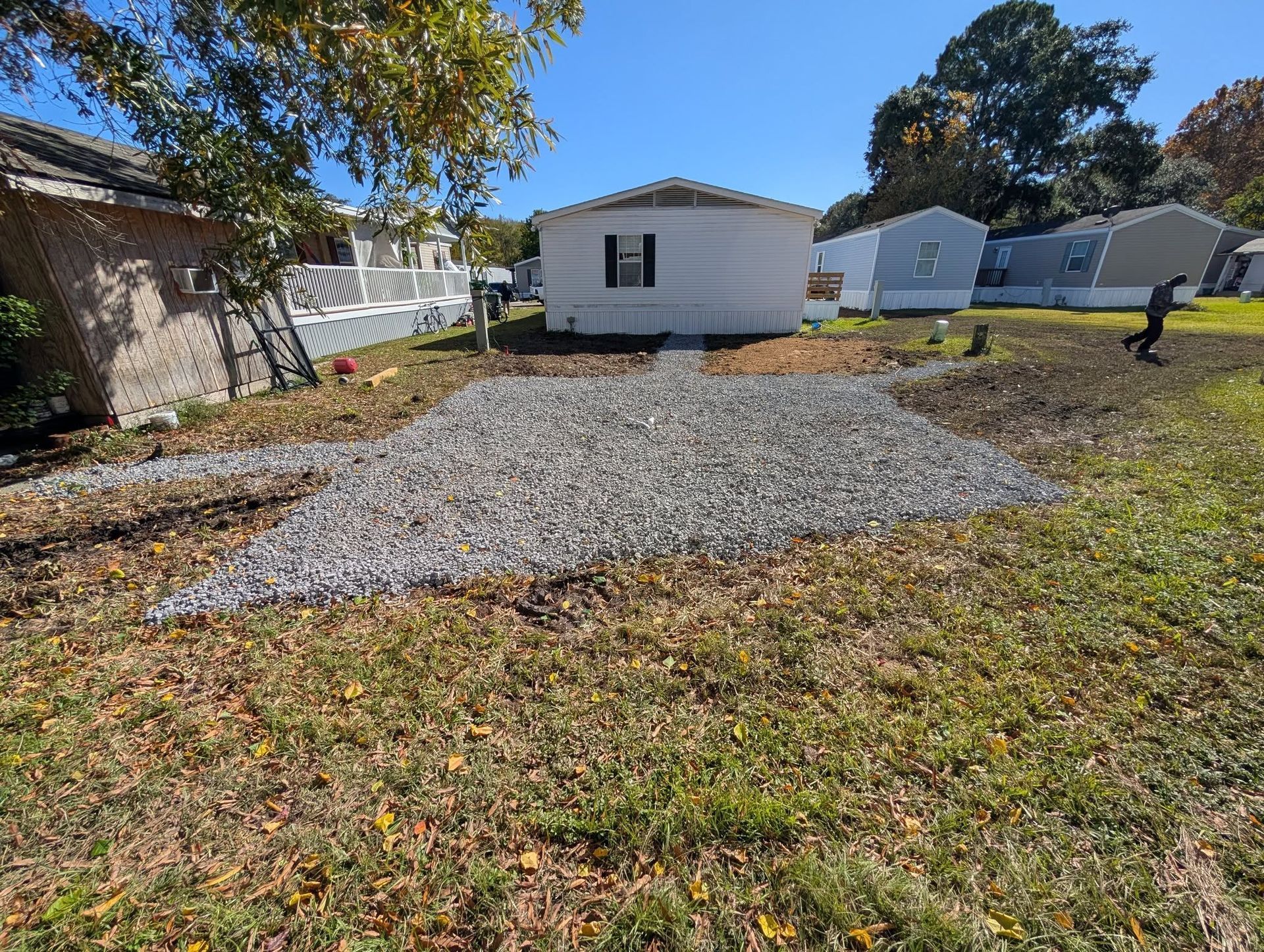 Gravel driveway in a backyard with a white shed and a person walking on the right.