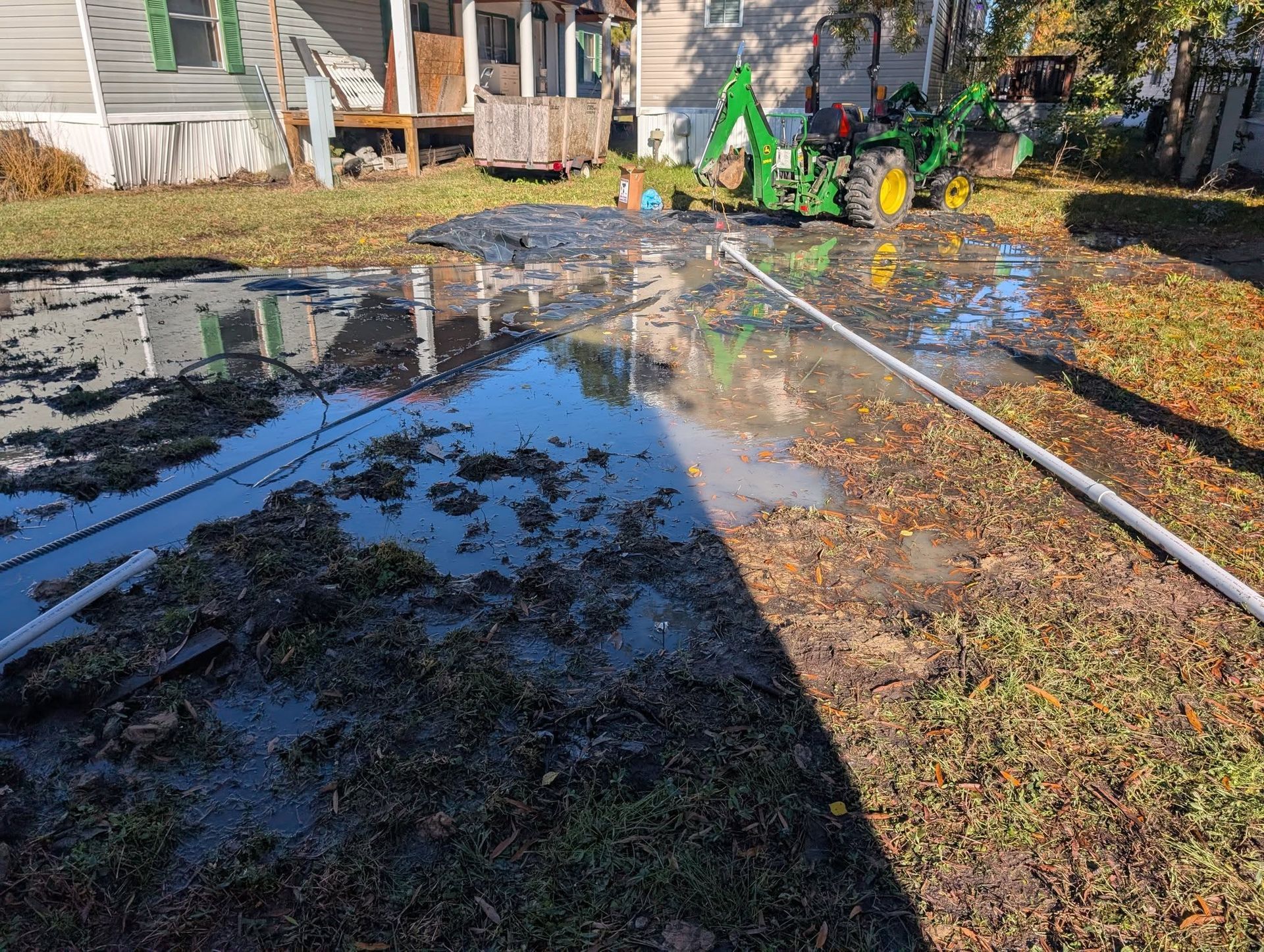Flooded backyard with standing water, fallen leaves, and a green excavator near a house