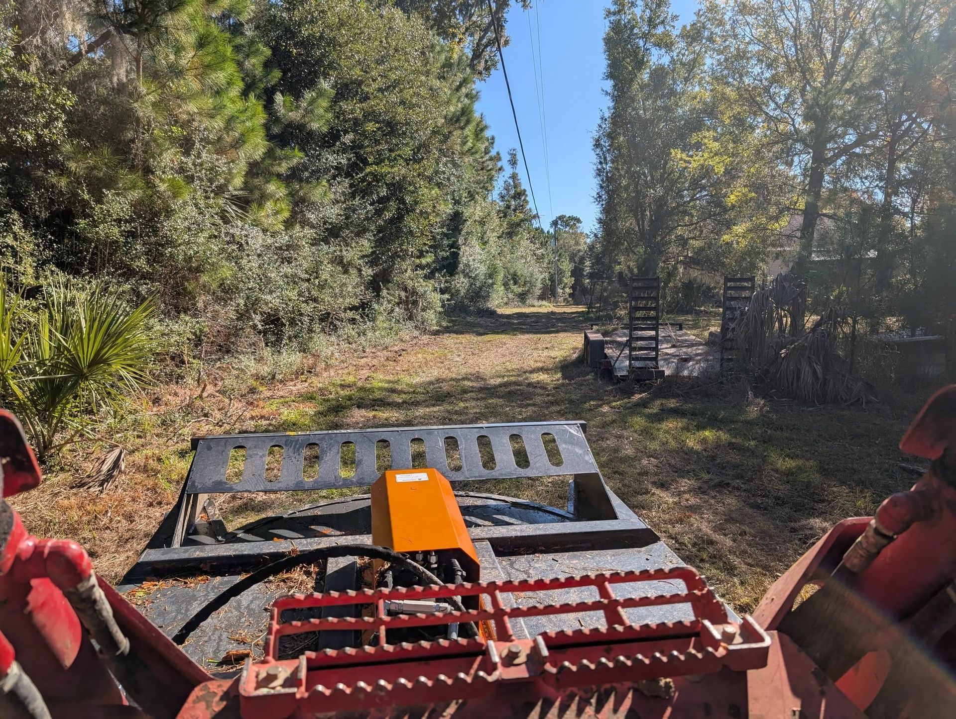Red off-road vehicle on a dirt trail, facing a wooded path under bright daylight.