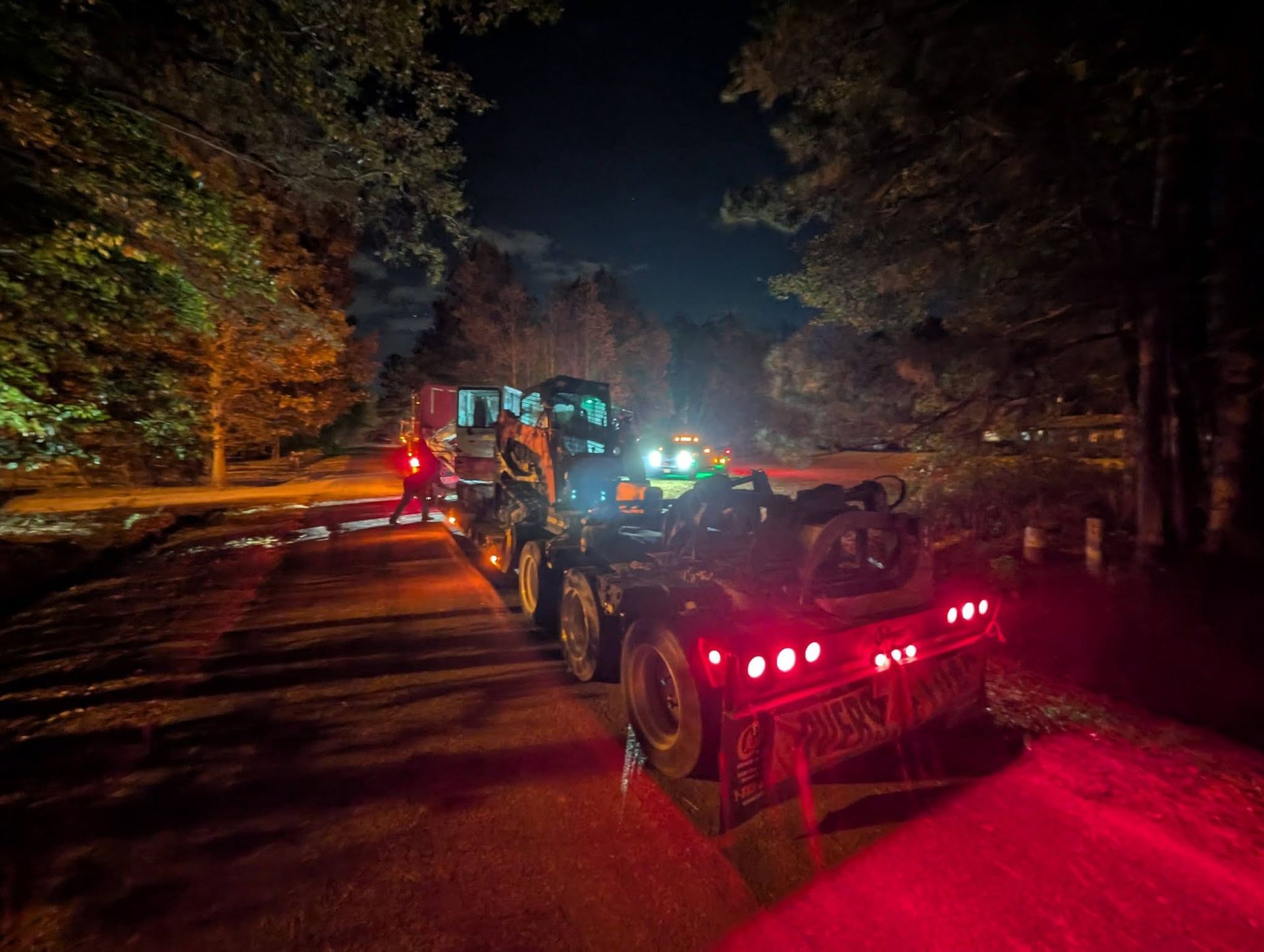 ATVs with red taillights line a dark wooded road at night