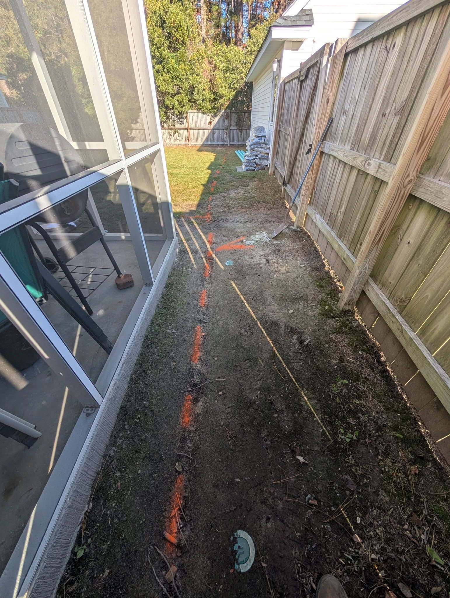 Narrow gravel path between a house and wooden fence, with orange spray markings on the ground.