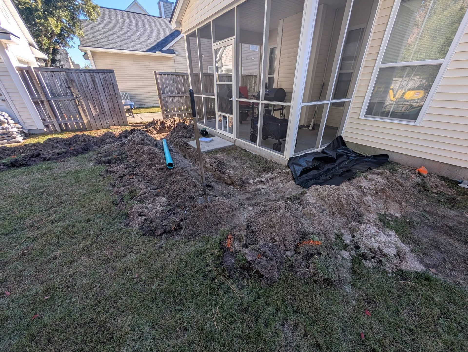 Backyard with freshly dug trench and soil beside a house and screened patio enclosure