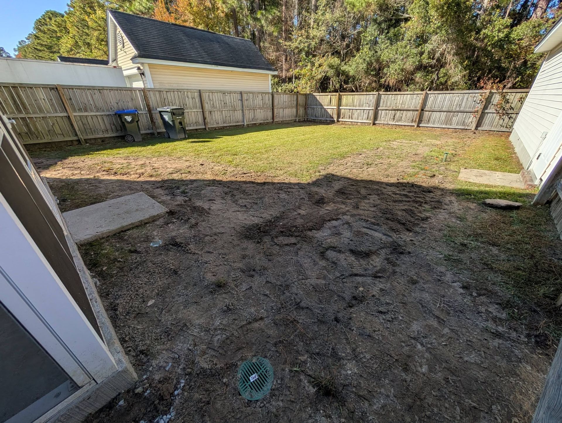 Backyard with patchy grass, fenced perimeter, and open sliding door in the foreground.