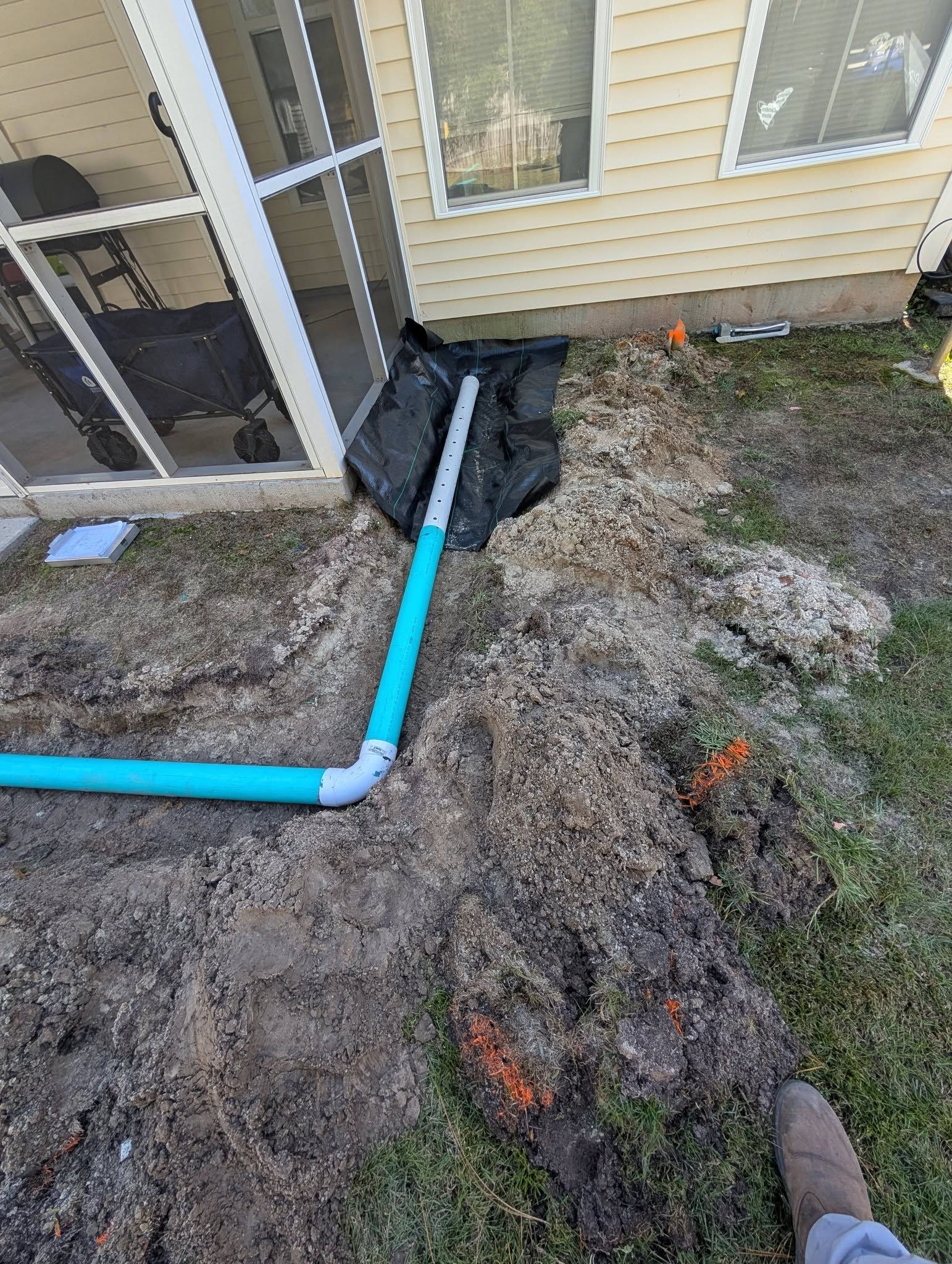 Blue PVC pipe along house foundation beside muddy, gravelly ground and a screened porch.
