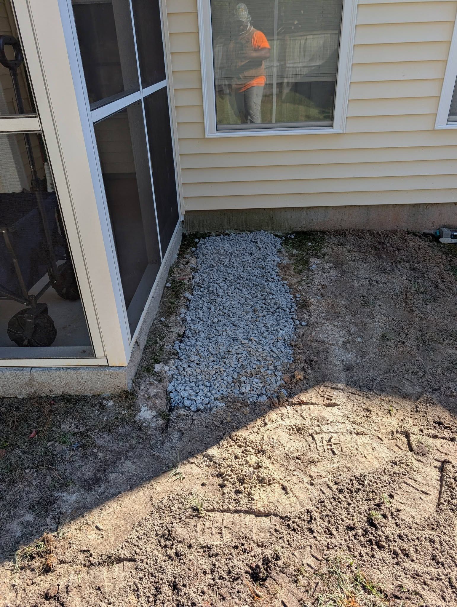 Backyard patio beside beige siding and windows, with screened door and a patch of snow on the ground