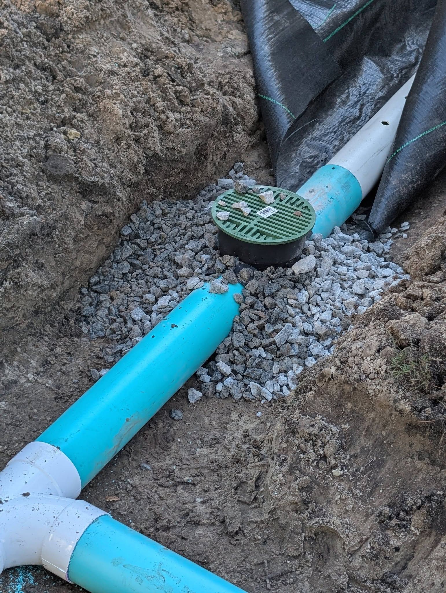 Blue utility pipes connected in a gravel trench between rocks, with a capped pipe end.