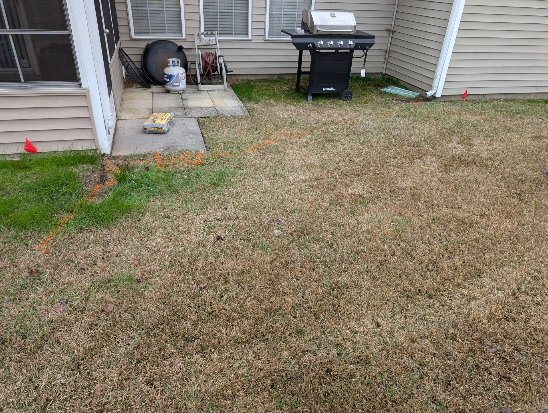 Backyard patio with a grill, concrete steps, and a patchy brown lawn.