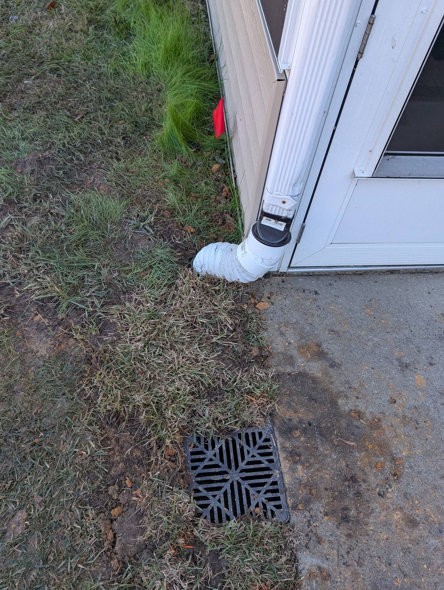 Downspout draining into a white extension beside a house, next to a lawn drain grate.