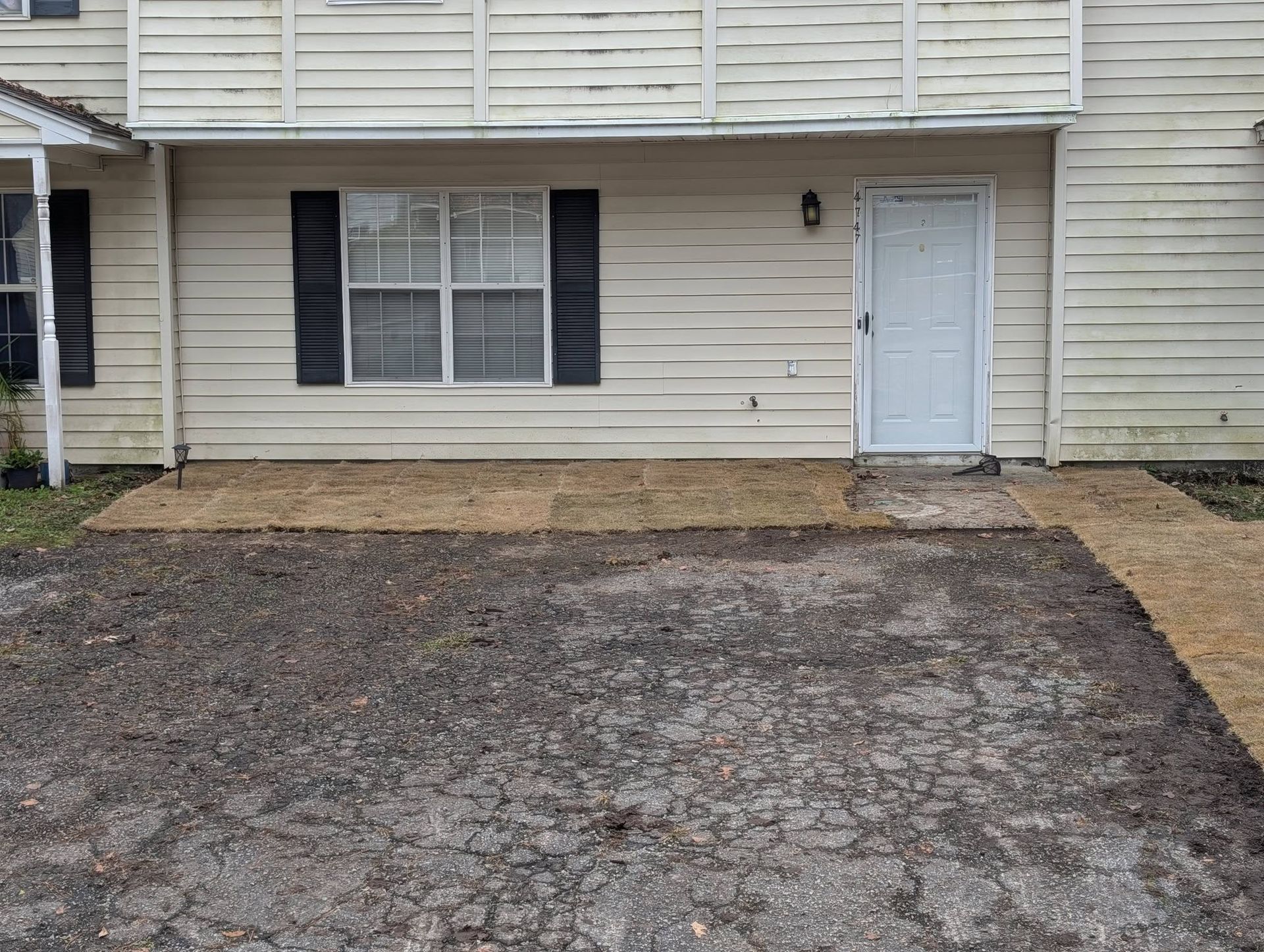 Front of beige townhouse with white door, window, and a gravel driveway or parking area.