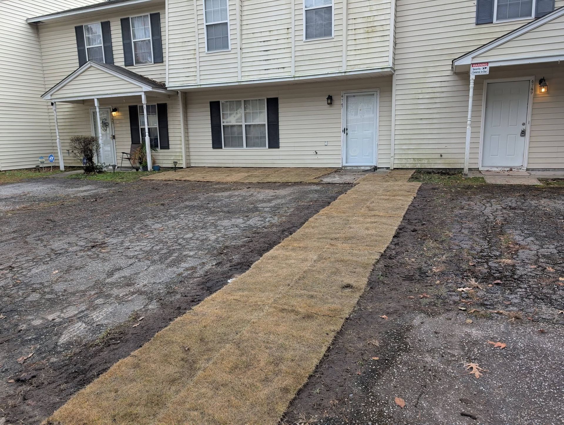 Front walkway leading to beige apartment entrances beside muddy, snow-dusted ground