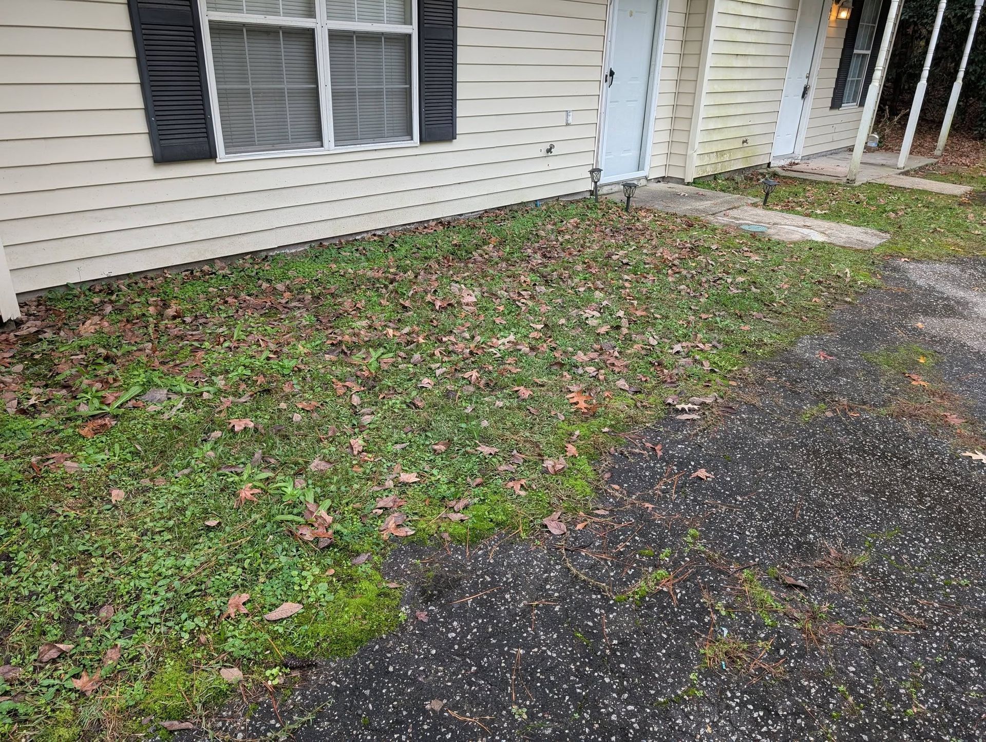 Side yard with patchy grass beside a white house, black shutters, and a gravel driveway.