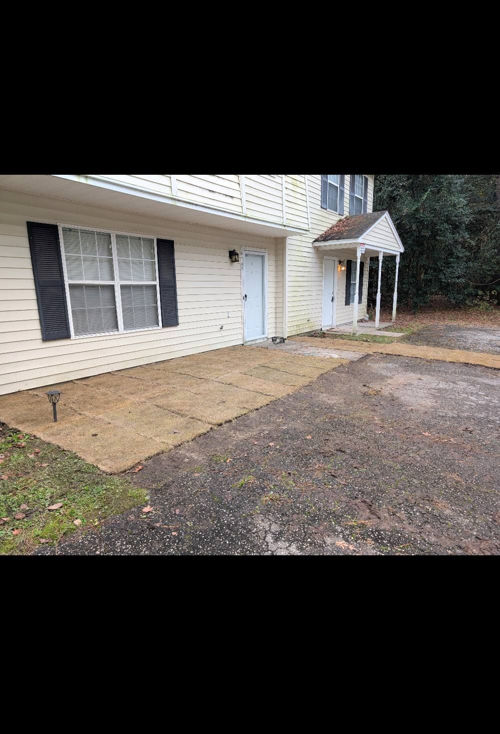 House exterior with beige siding, front door, windows, small porch, and gravel driveway after rain