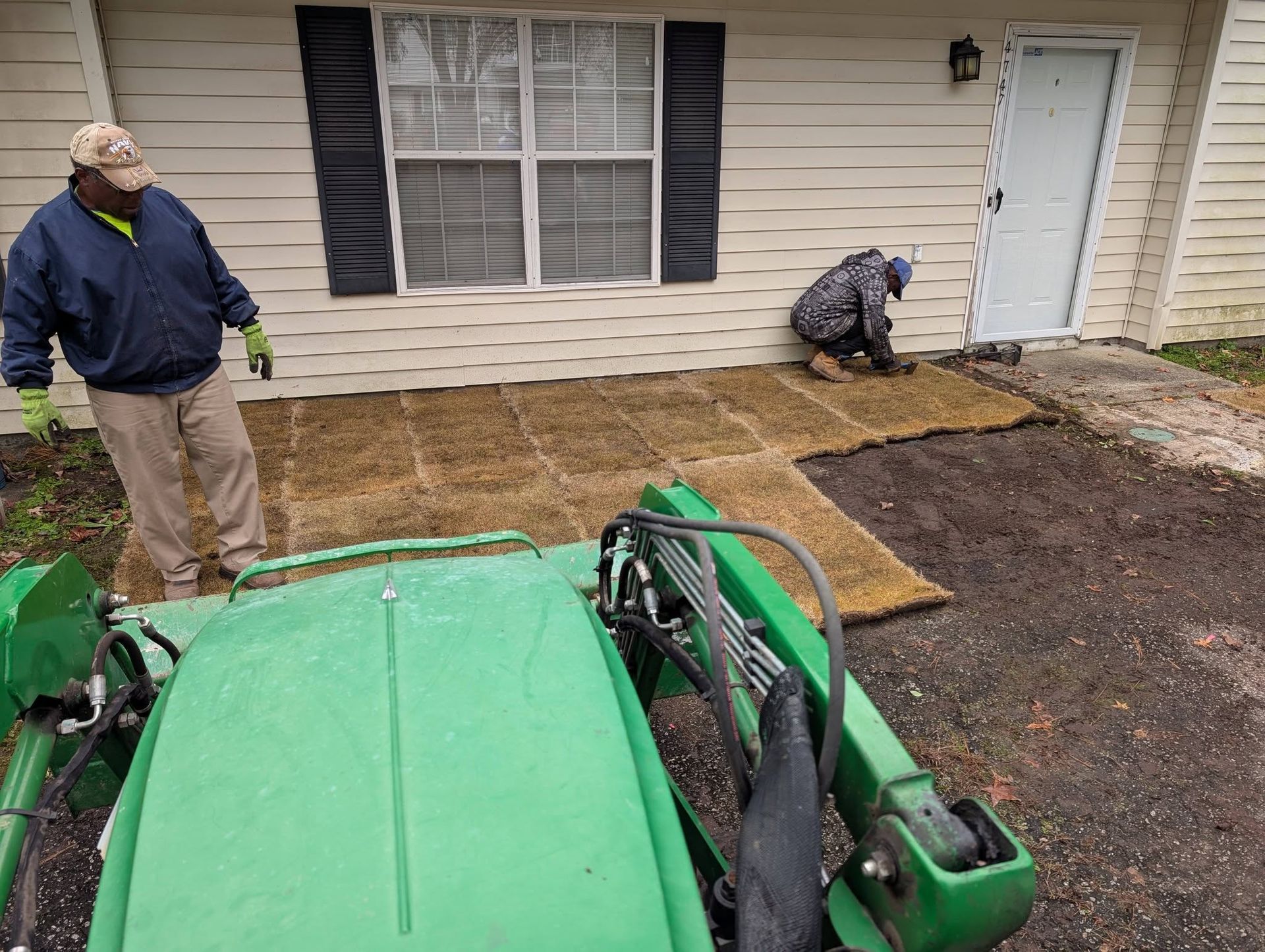 Two workers installing sod beside a house, with a green lawn mower in the foreground.