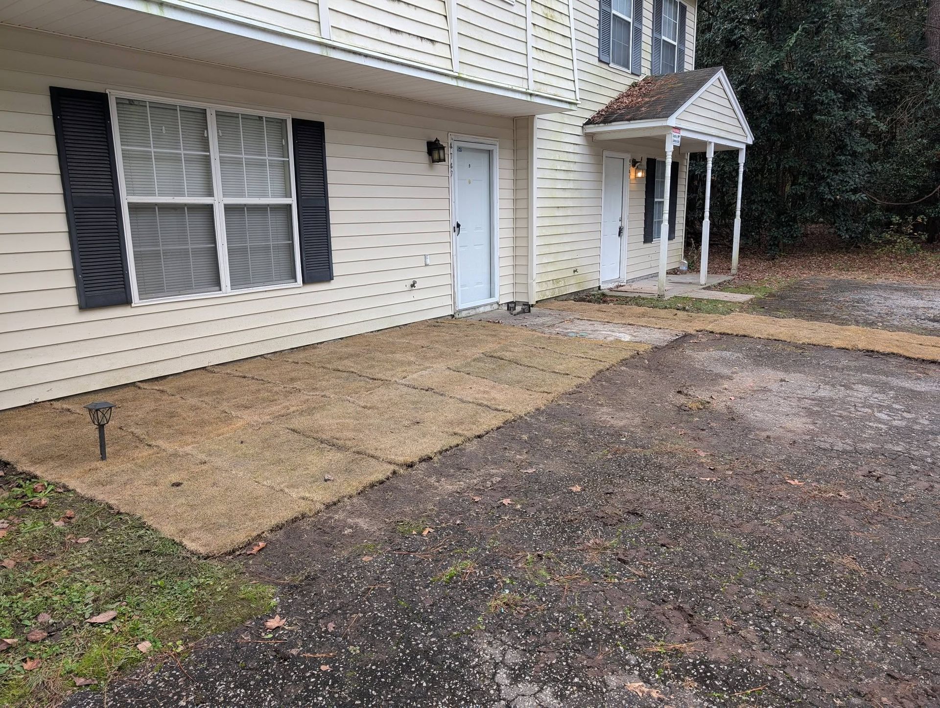 Apartment building exterior with white siding, black shutters, and a paved driveway in front