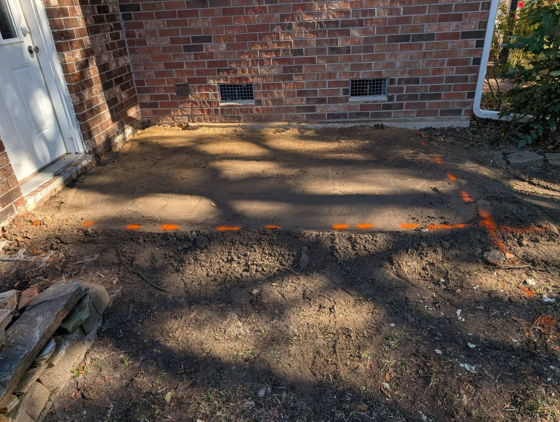Cracked concrete driveway beside a brick wall and white door, with shadows across the ground.