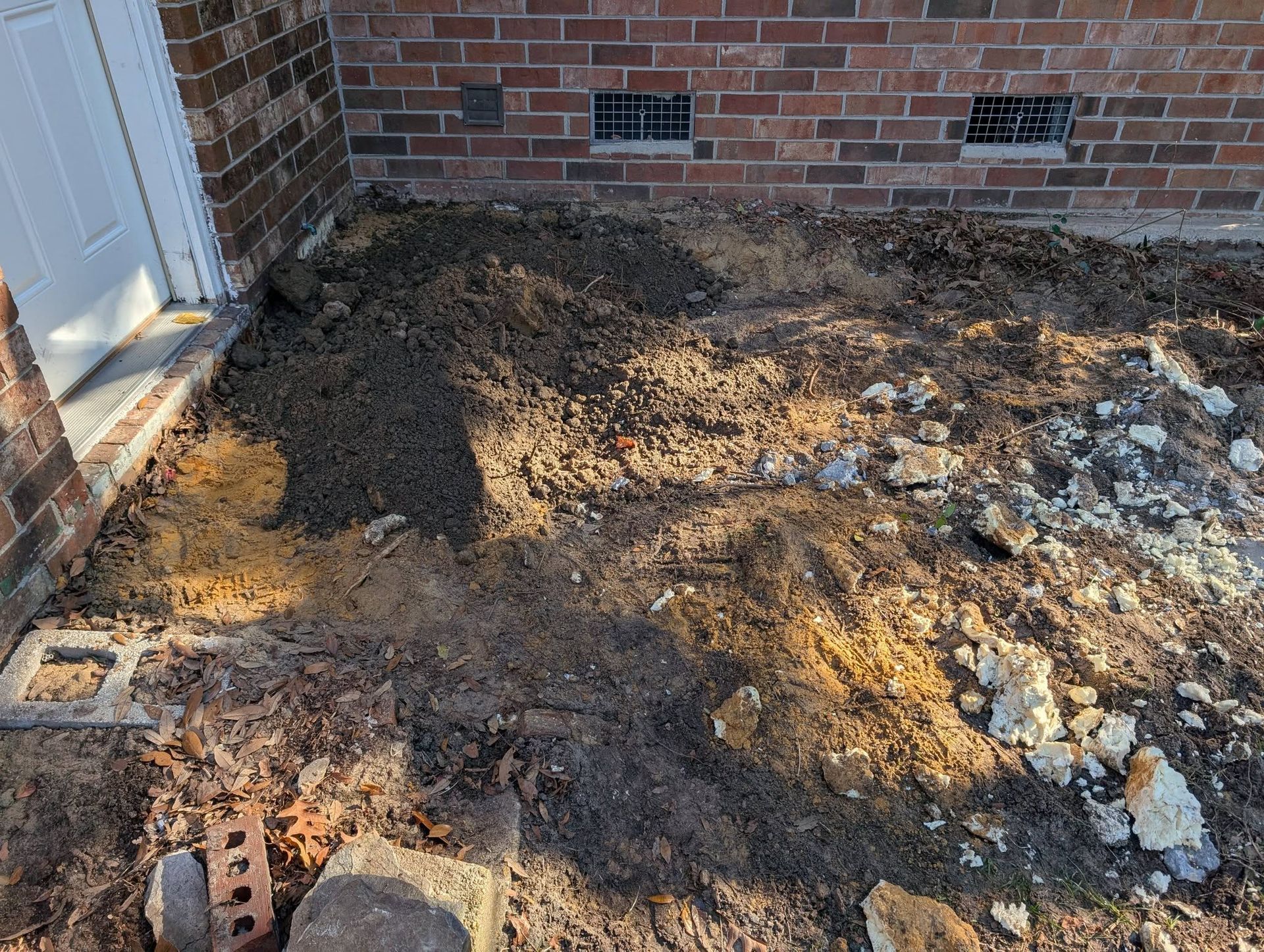 Mud and dirt piled beside a brick house near a doorway, with scattered debris on the ground.