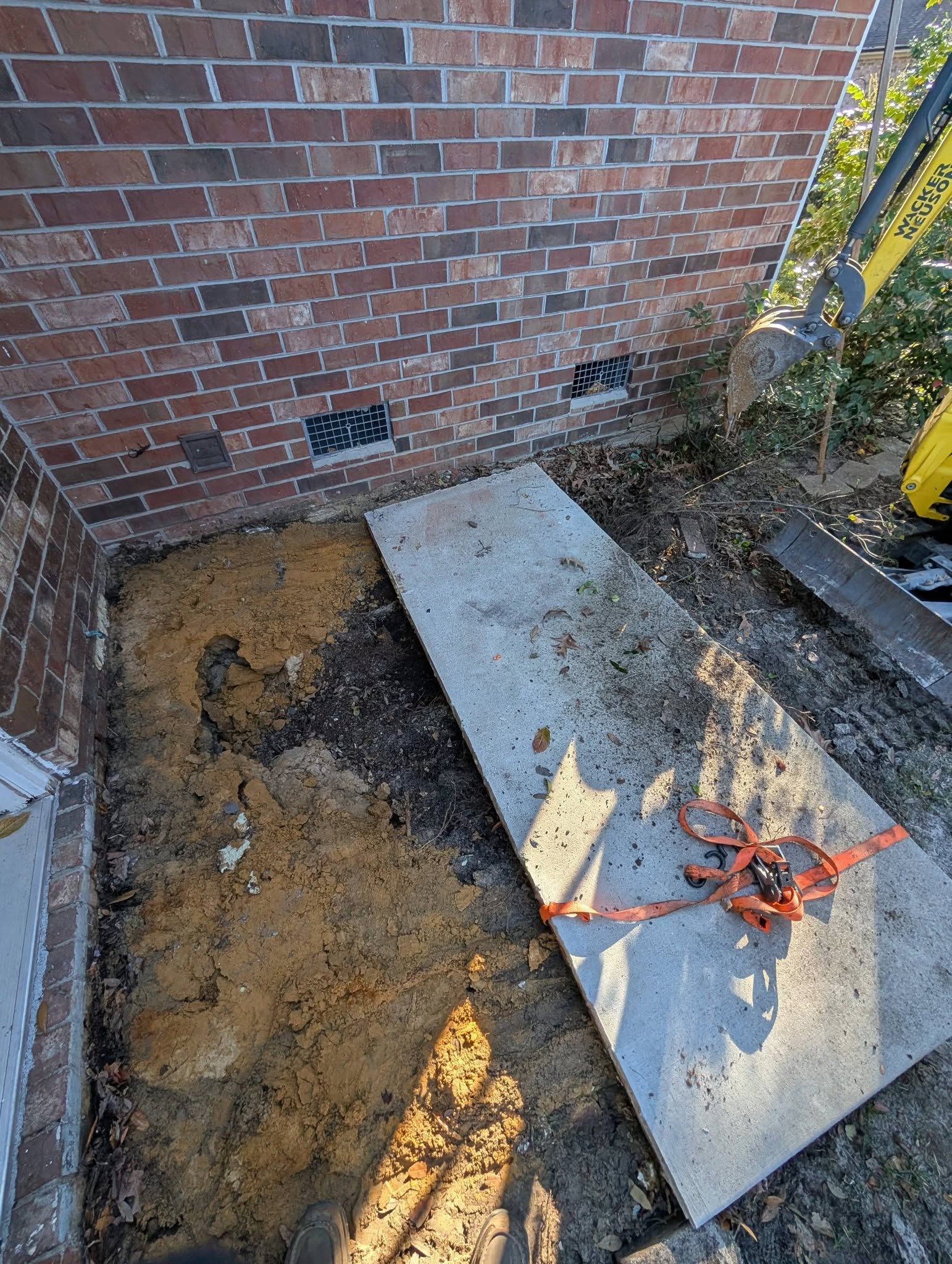 Broken concrete slab beside a brick wall, with dirt exposed and a red cable on the slab
