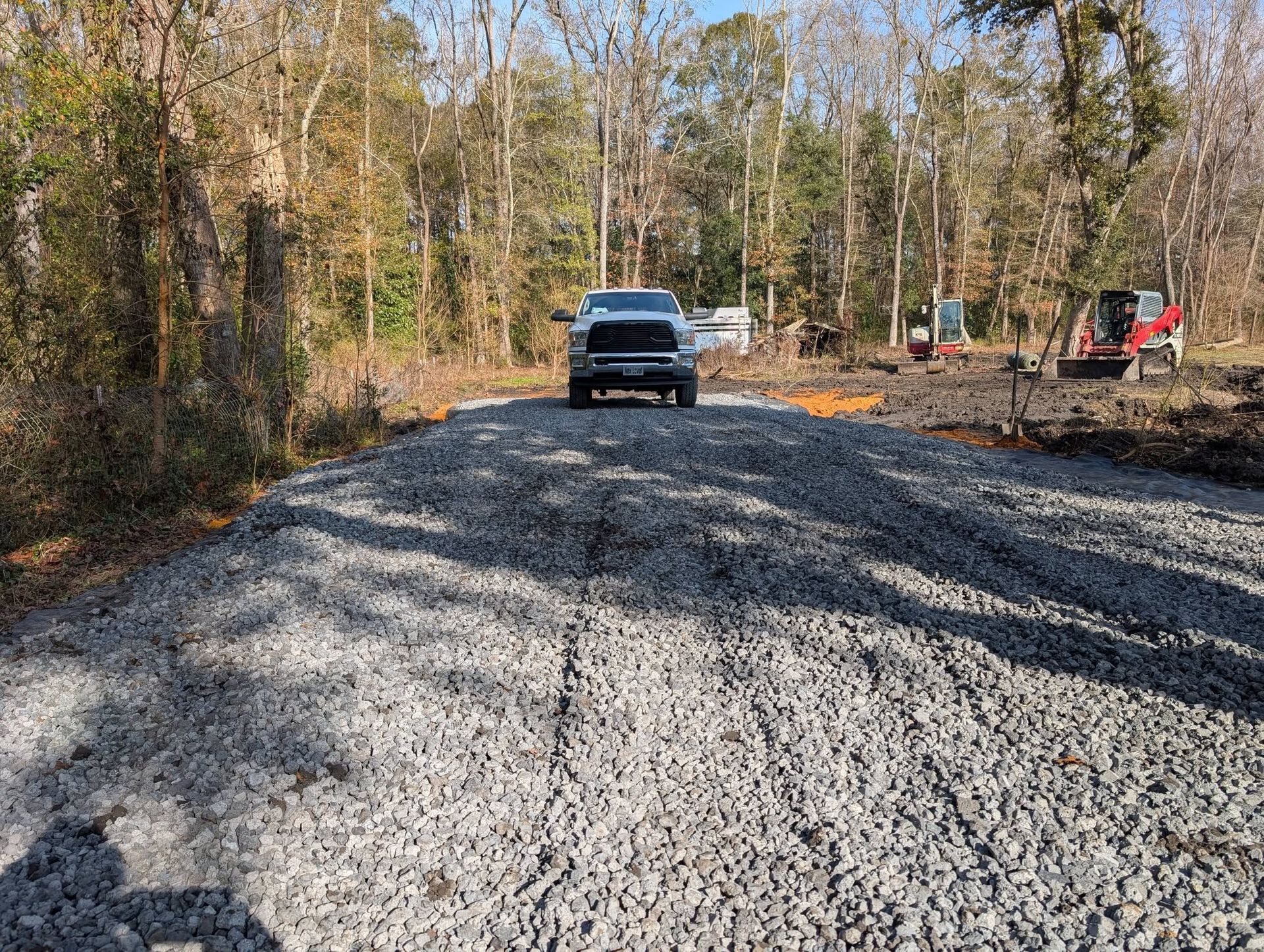 Gravel road under construction with a pickup truck and excavator in a wooded area