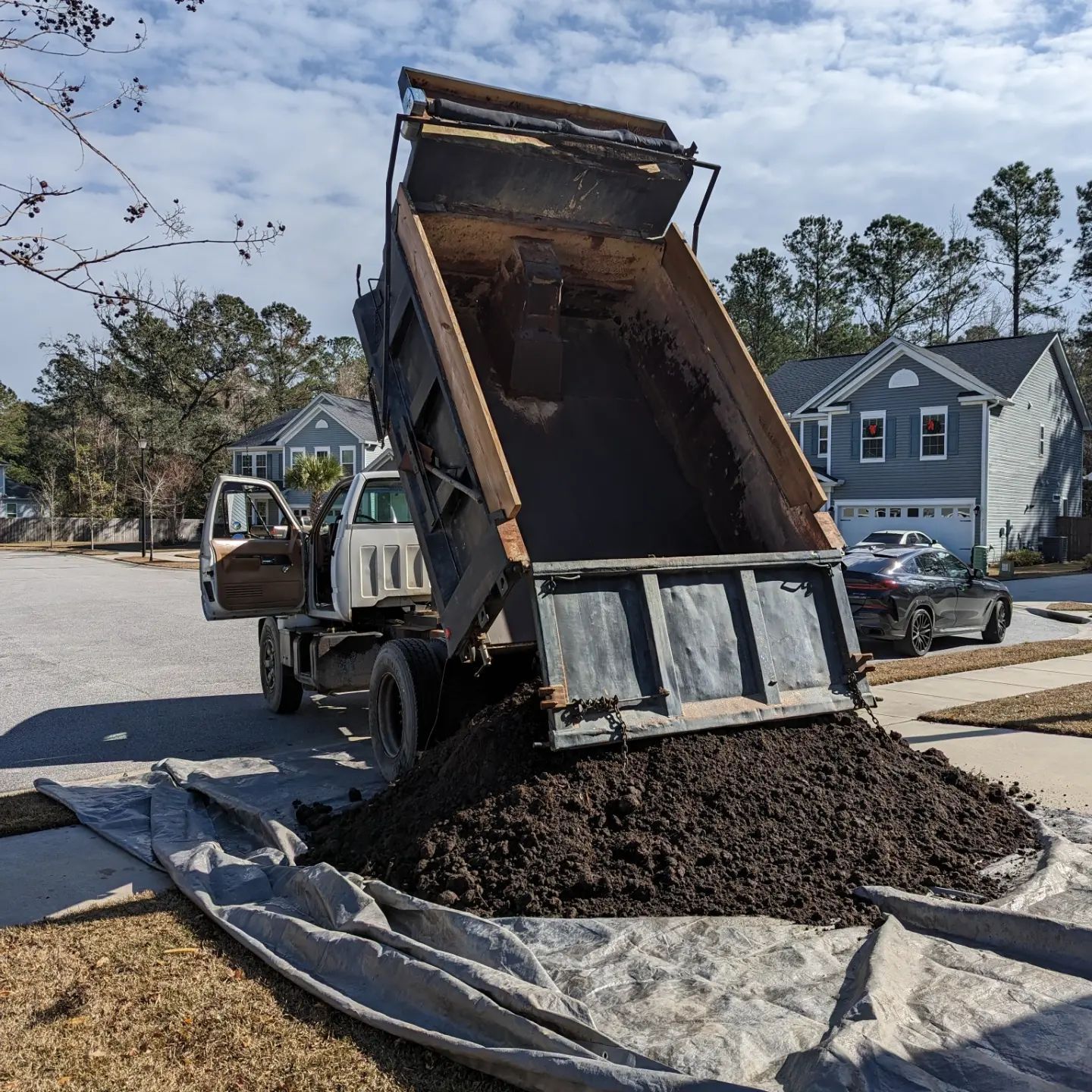 Dump truck unloading dark mulch onto a tarp in a residential driveway