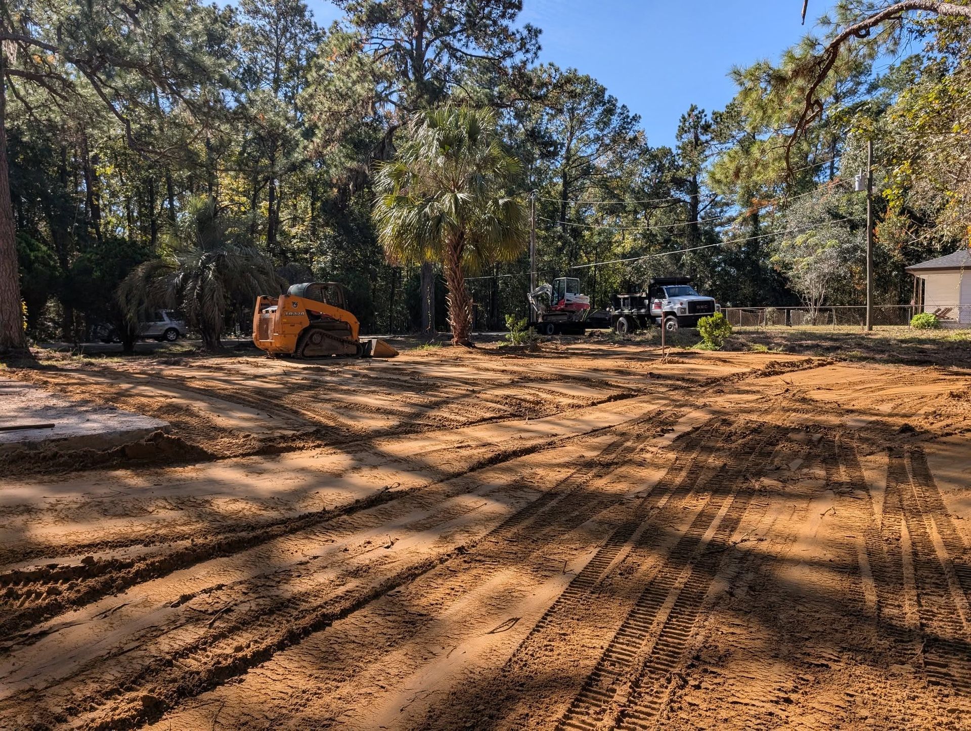 Cleared dirt lot with construction tracks, an orange excavator, and trees in the background