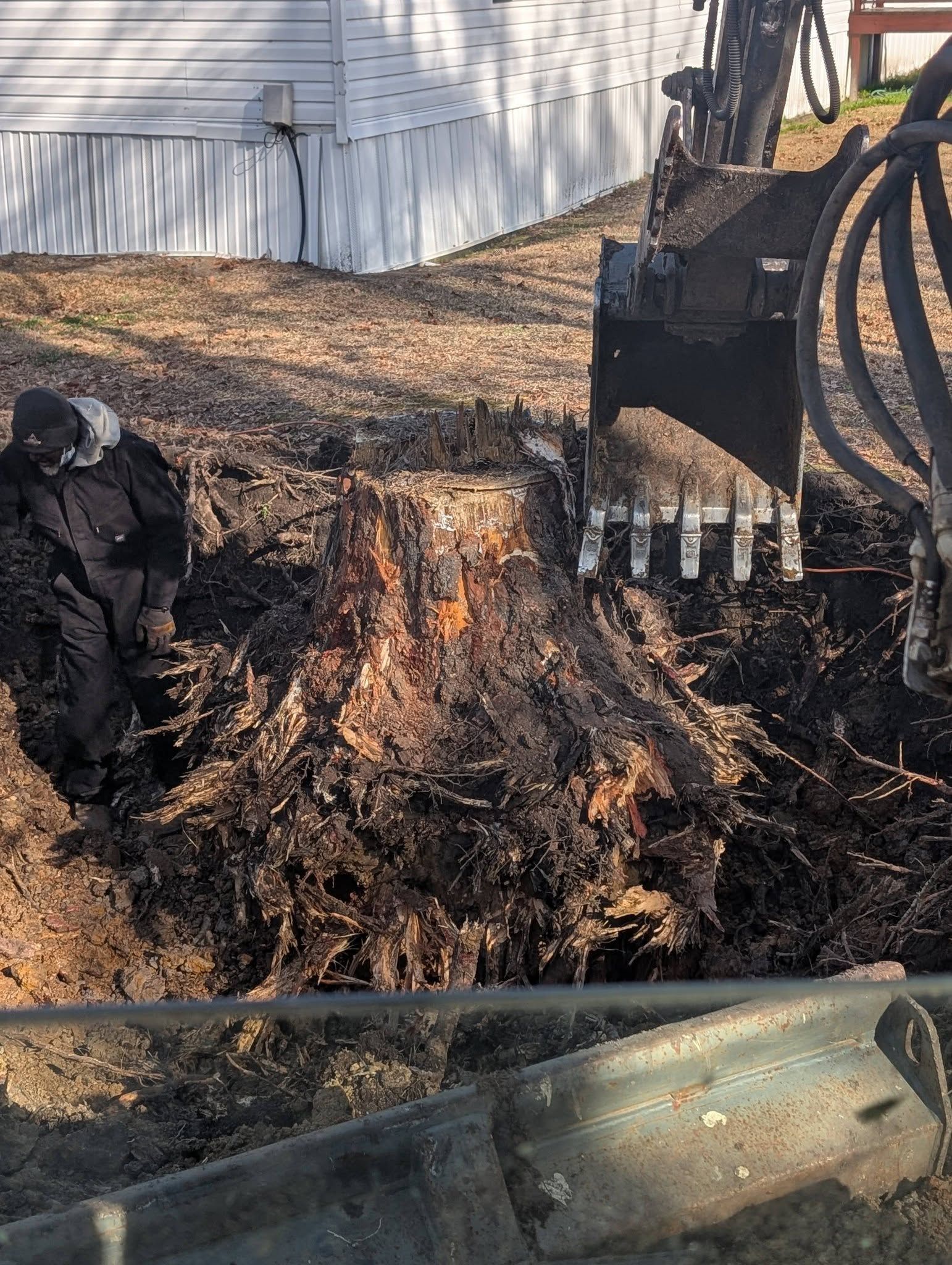 Close-up of muddy ground with a tracked machine and hose beside a white building.