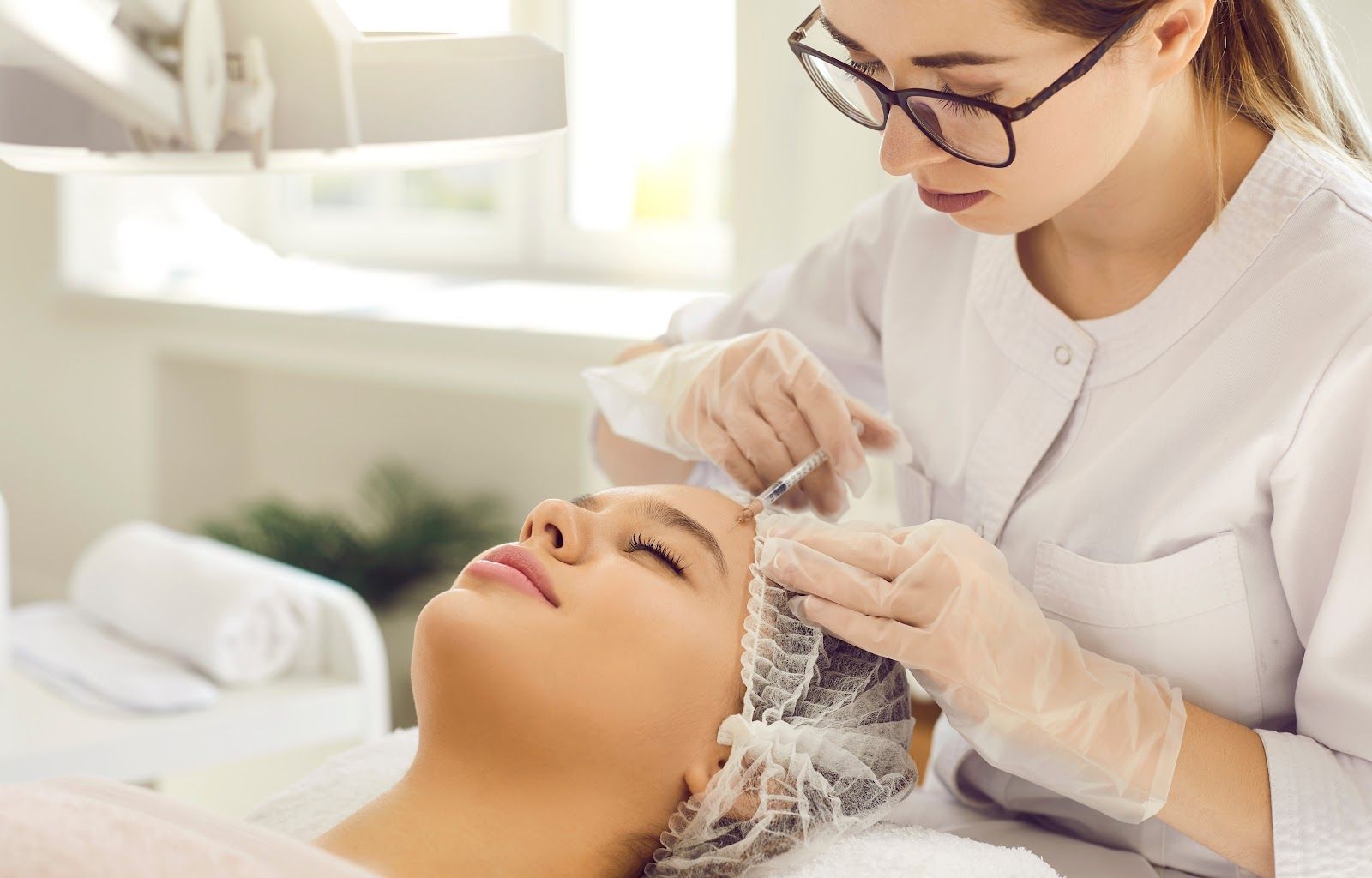 A skincare specialist applying treatment to a client’s face in a bright spa treatment room