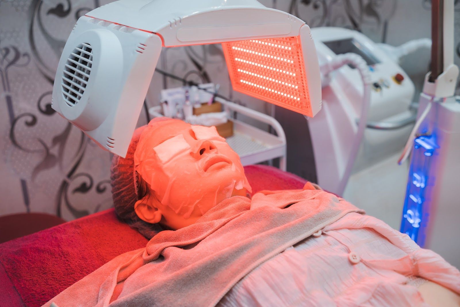Person receiving red light therapy under a treatment lamp while lying on a bed