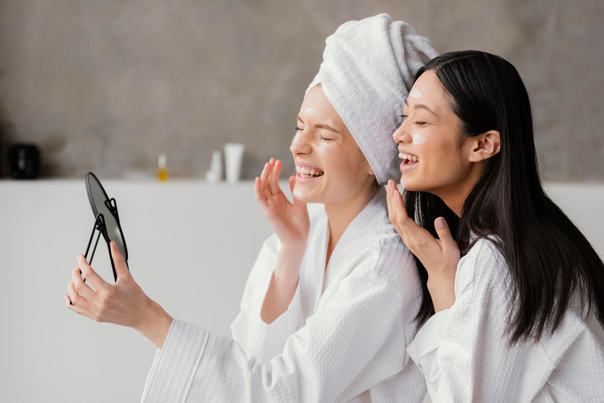 Two people in white robes taking a selfie, smiling in a bright spa setting