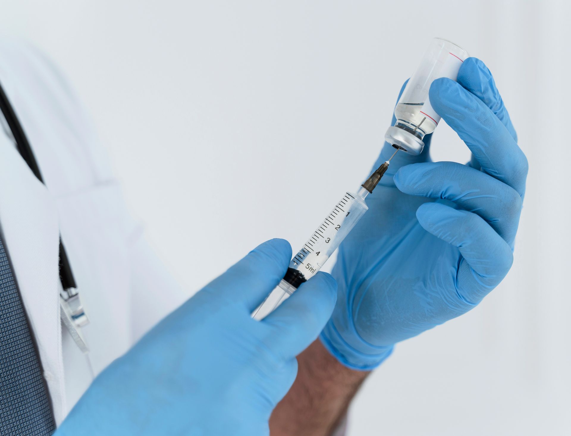 Blue-gloved hands drawing medication into a syringe in a clinical setting