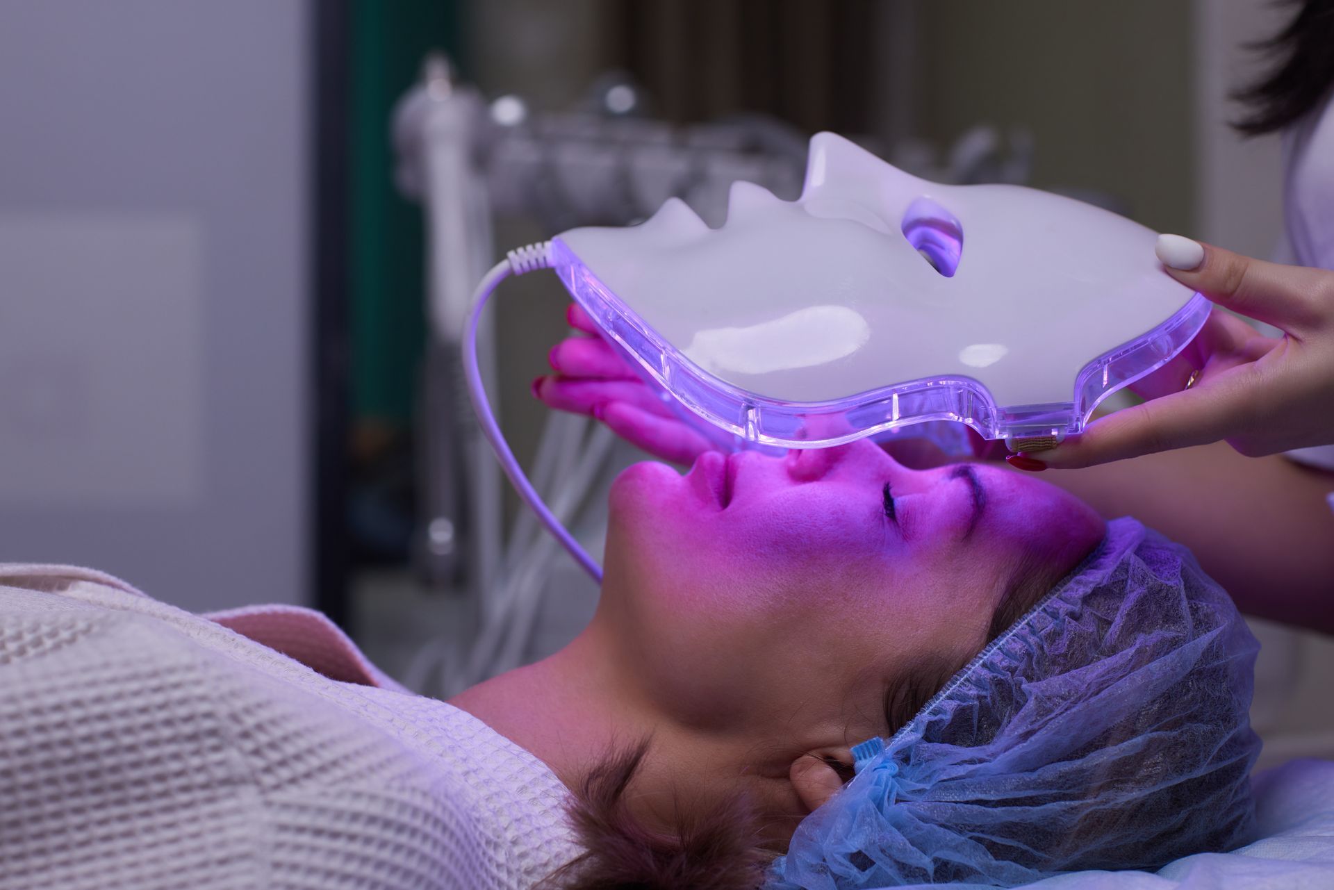 Woman receiving LED light facial therapy in a spa treatment room