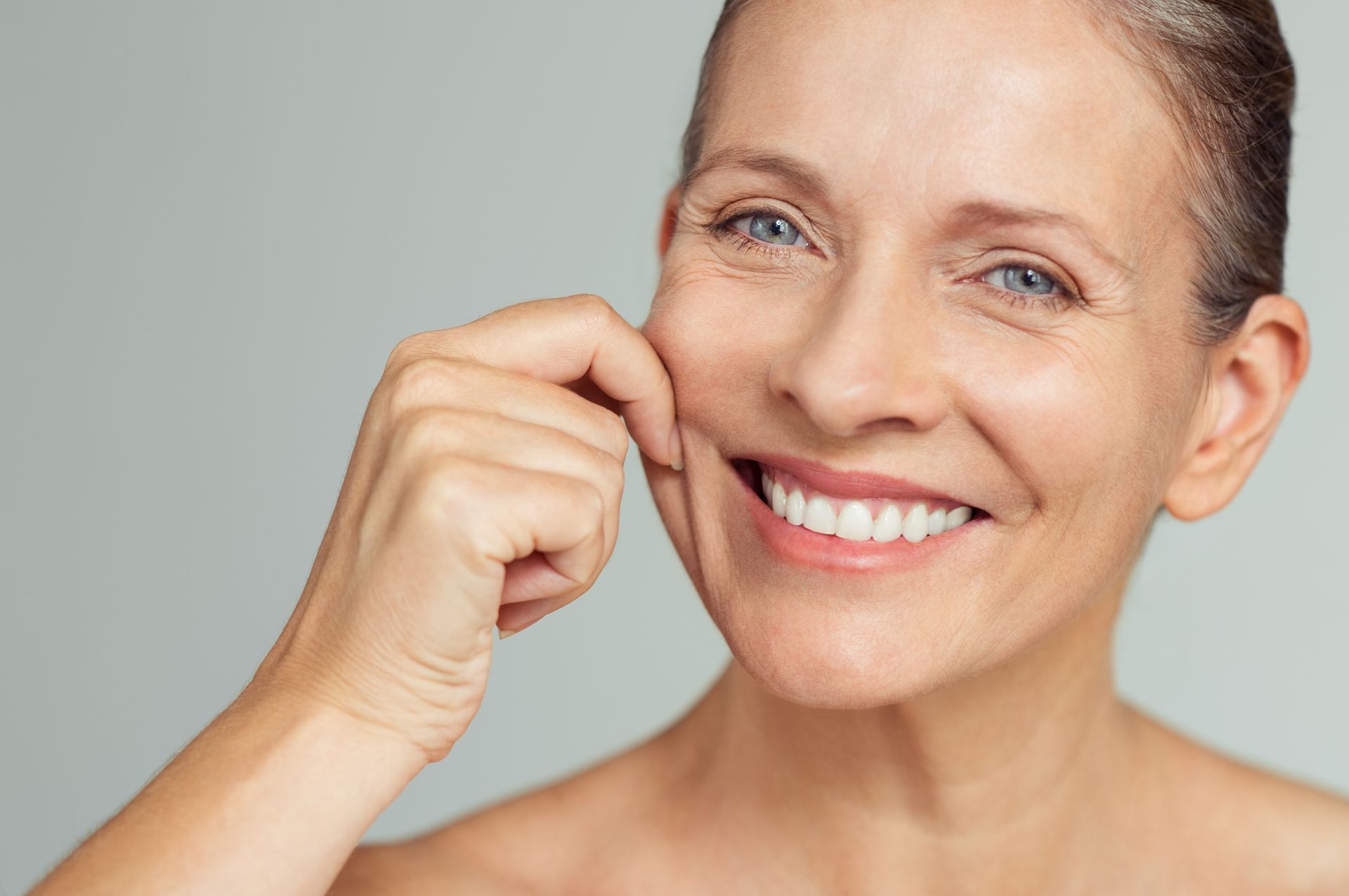 Smiling person touching their cheek against a light gray background