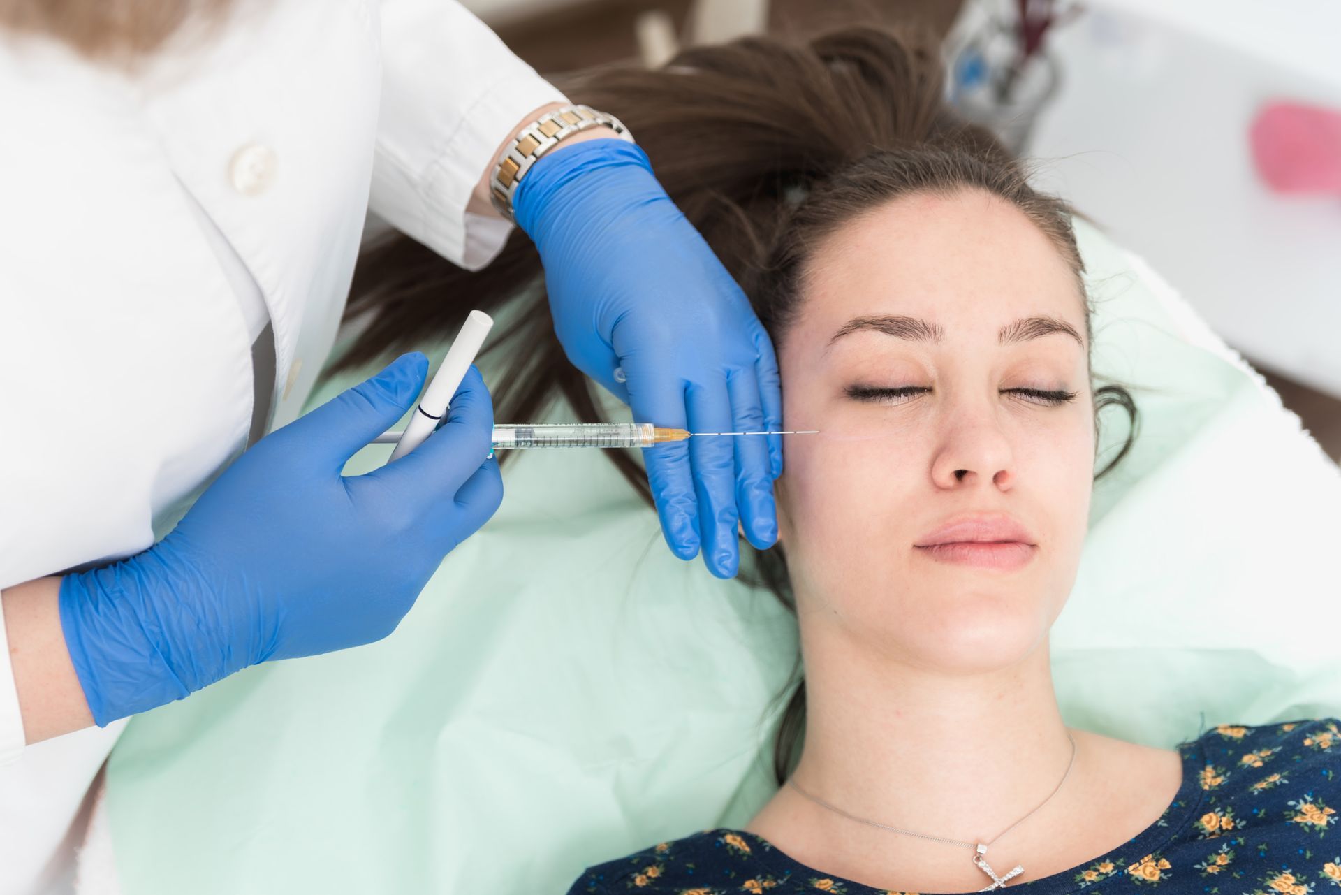 Aesthetic treatment being injected into a woman's face as she lies with eyes closed on a medical bed