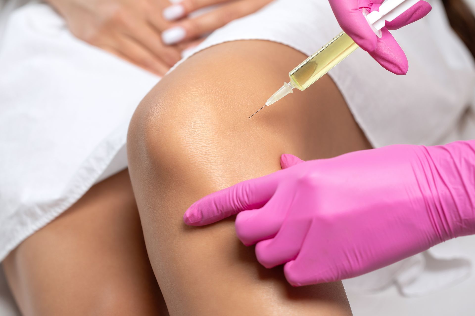 Gloved hands administering an injection into a patient’s knee during a medical procedure