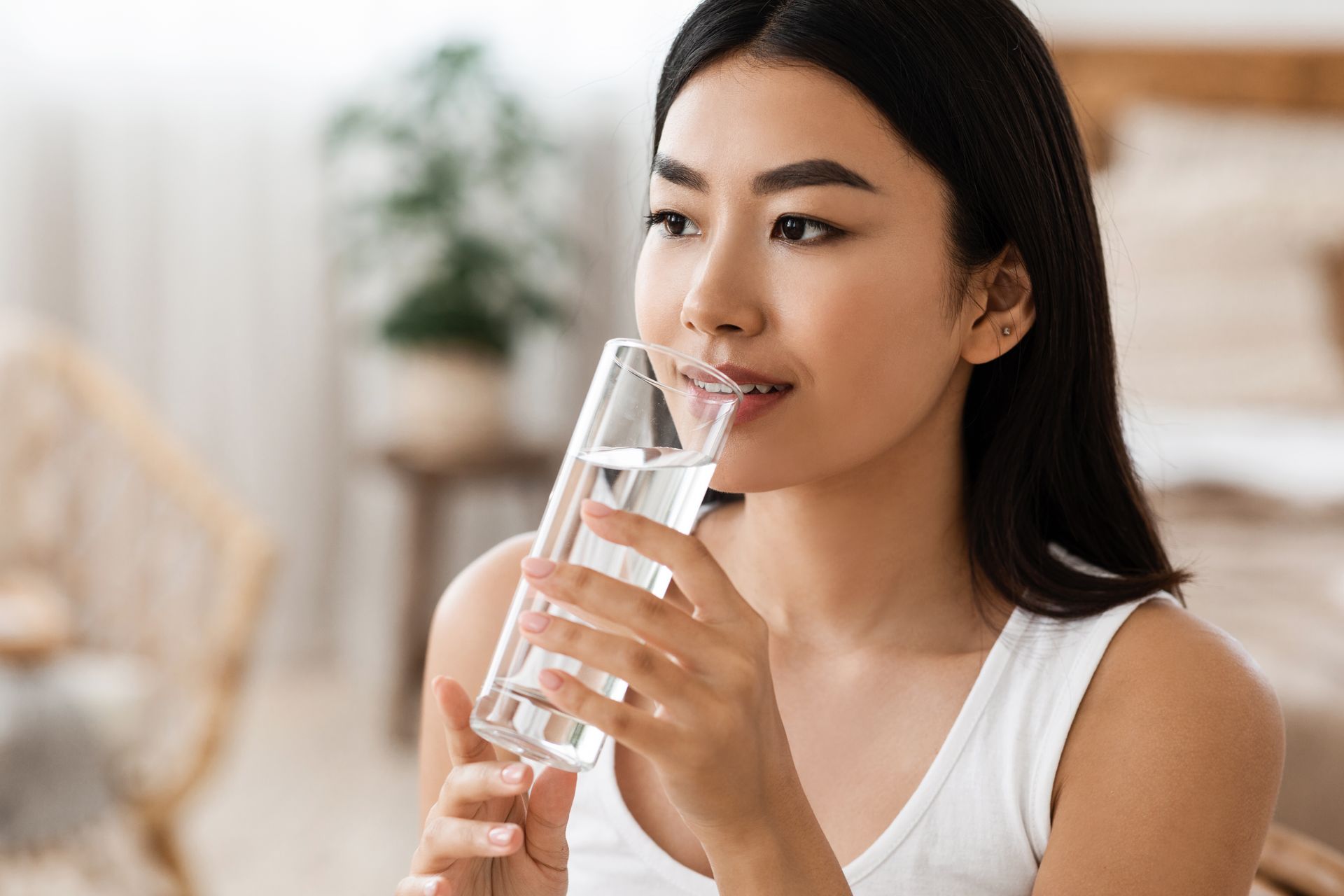 Woman drinking water from a glass in a bright indoor setting