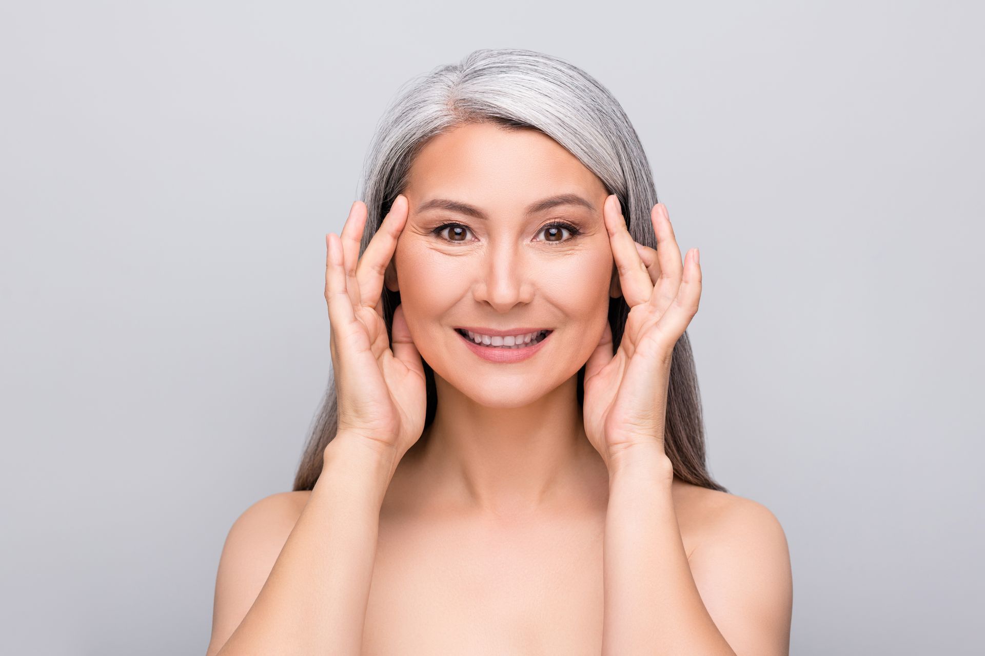 Smiling silver-haired woman with hands near her face against a light gray background