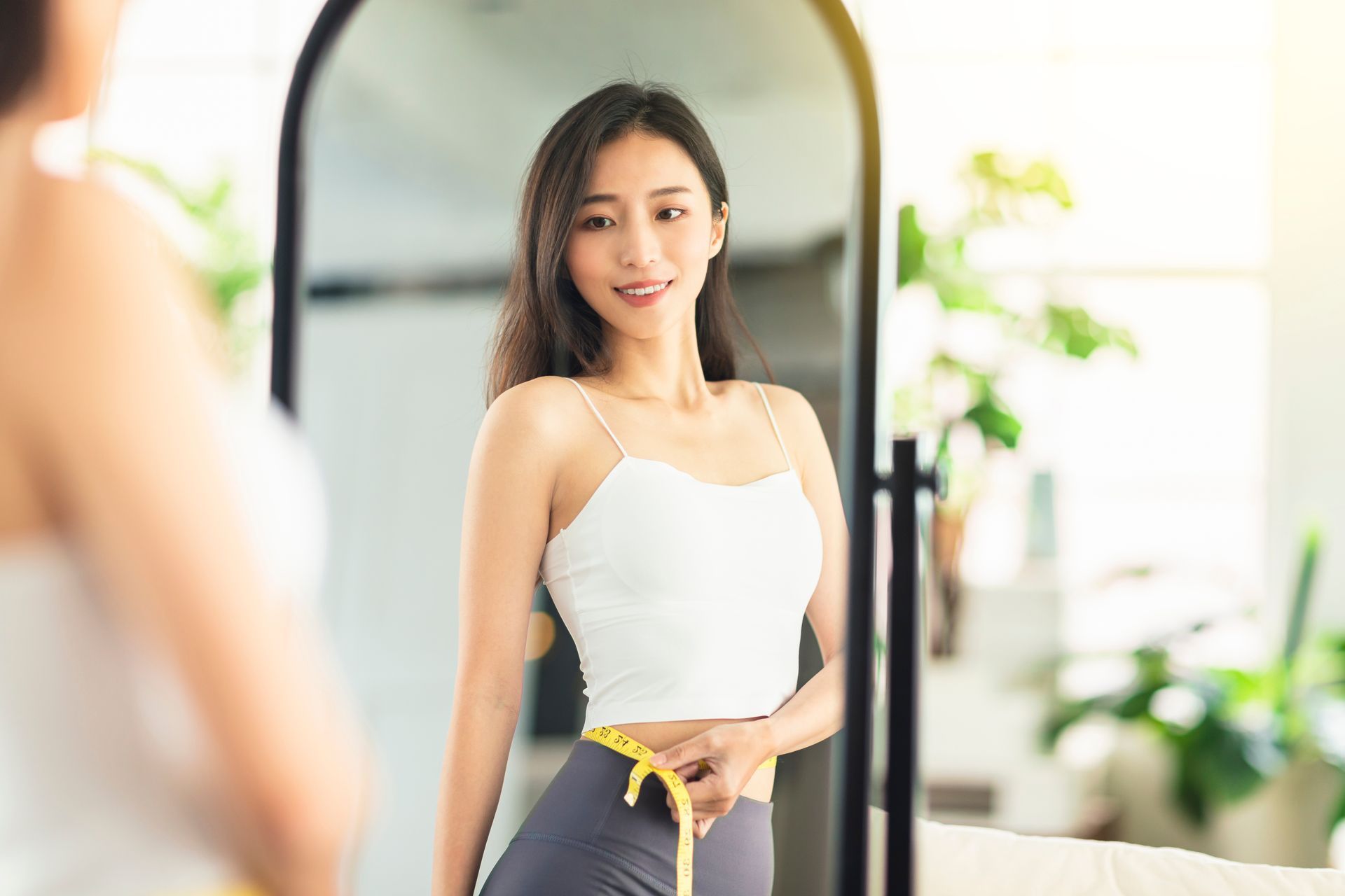 Woman in a white top posing in front of a mirror in a bright room.