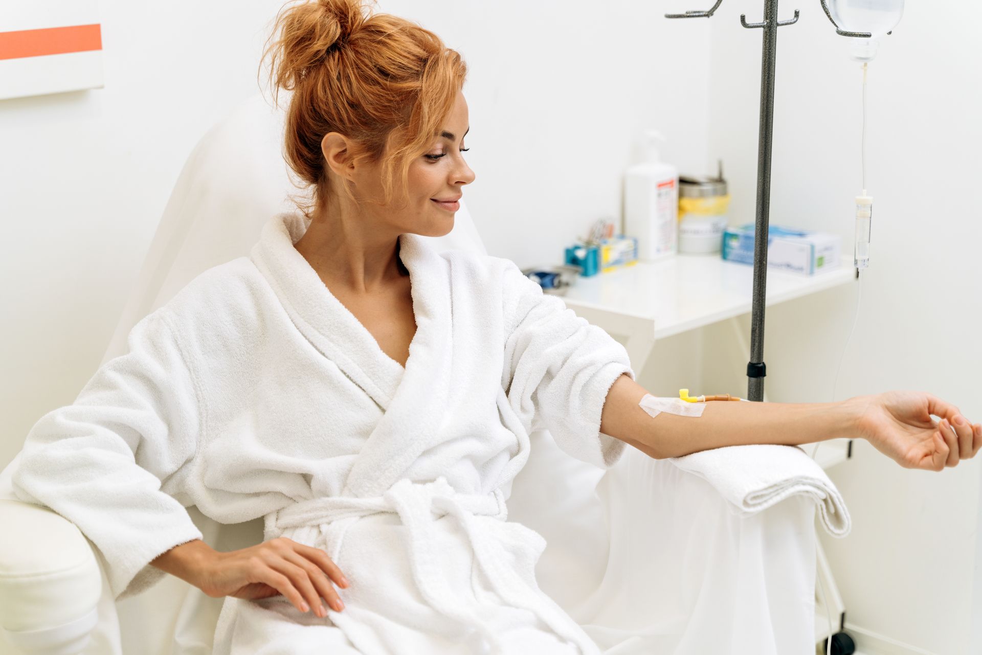 Woman in a white robe seated in a clinic, extending her arm for a blood test or IV.
