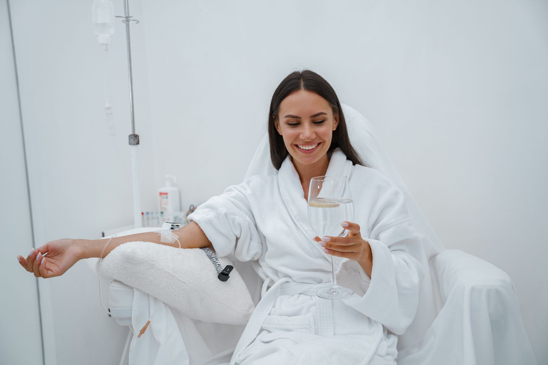 Woman in a white robe smiling while holding a drink in a bright spa room