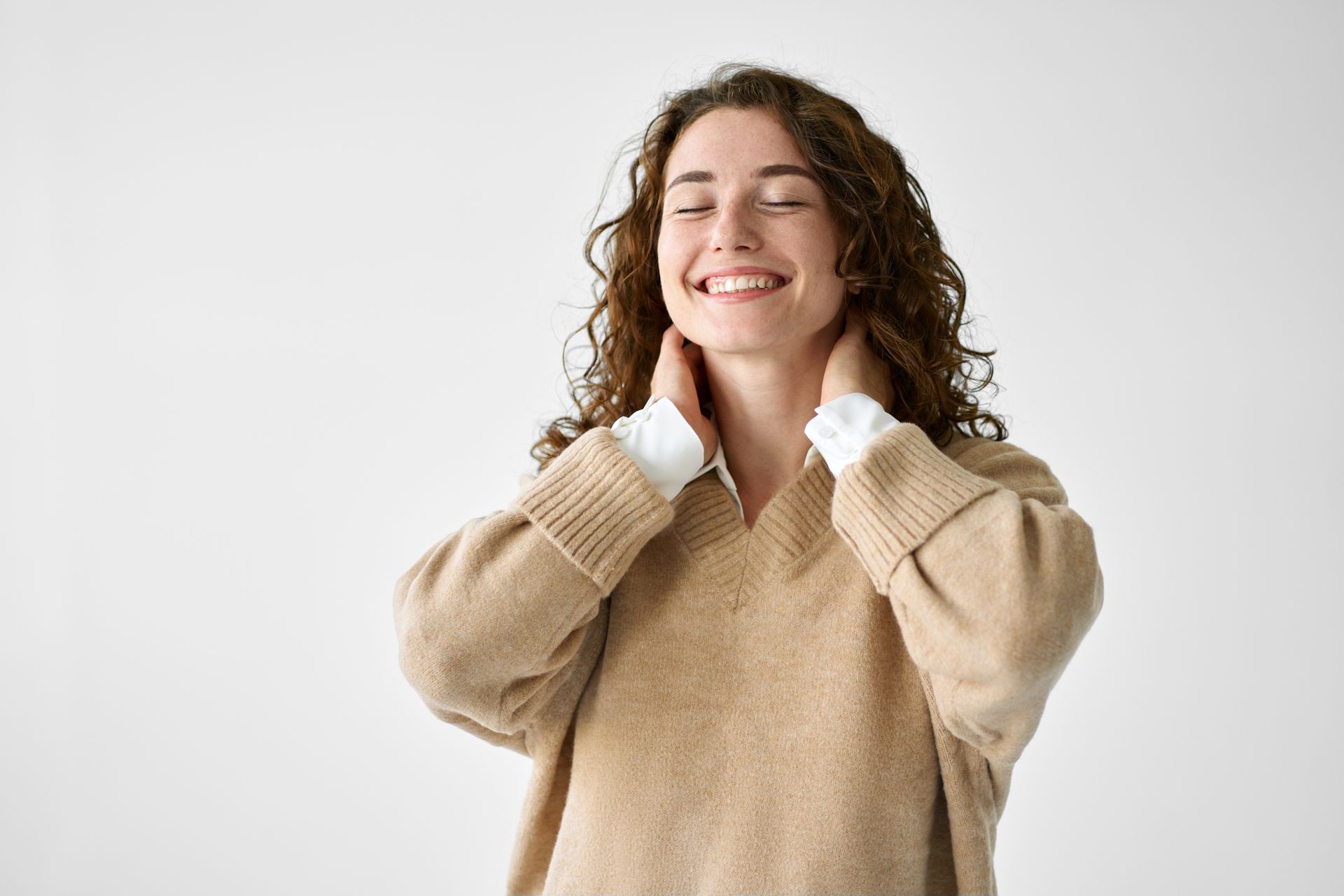 Smiling person in beige sweater holding their collar against a white background