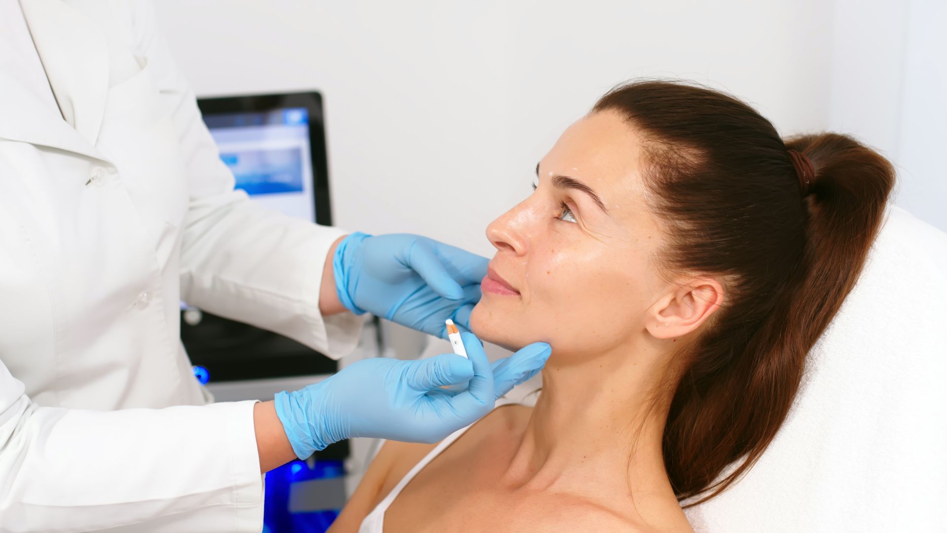 Medical professional examining a patient’s face with gloved hands in a clinic setting