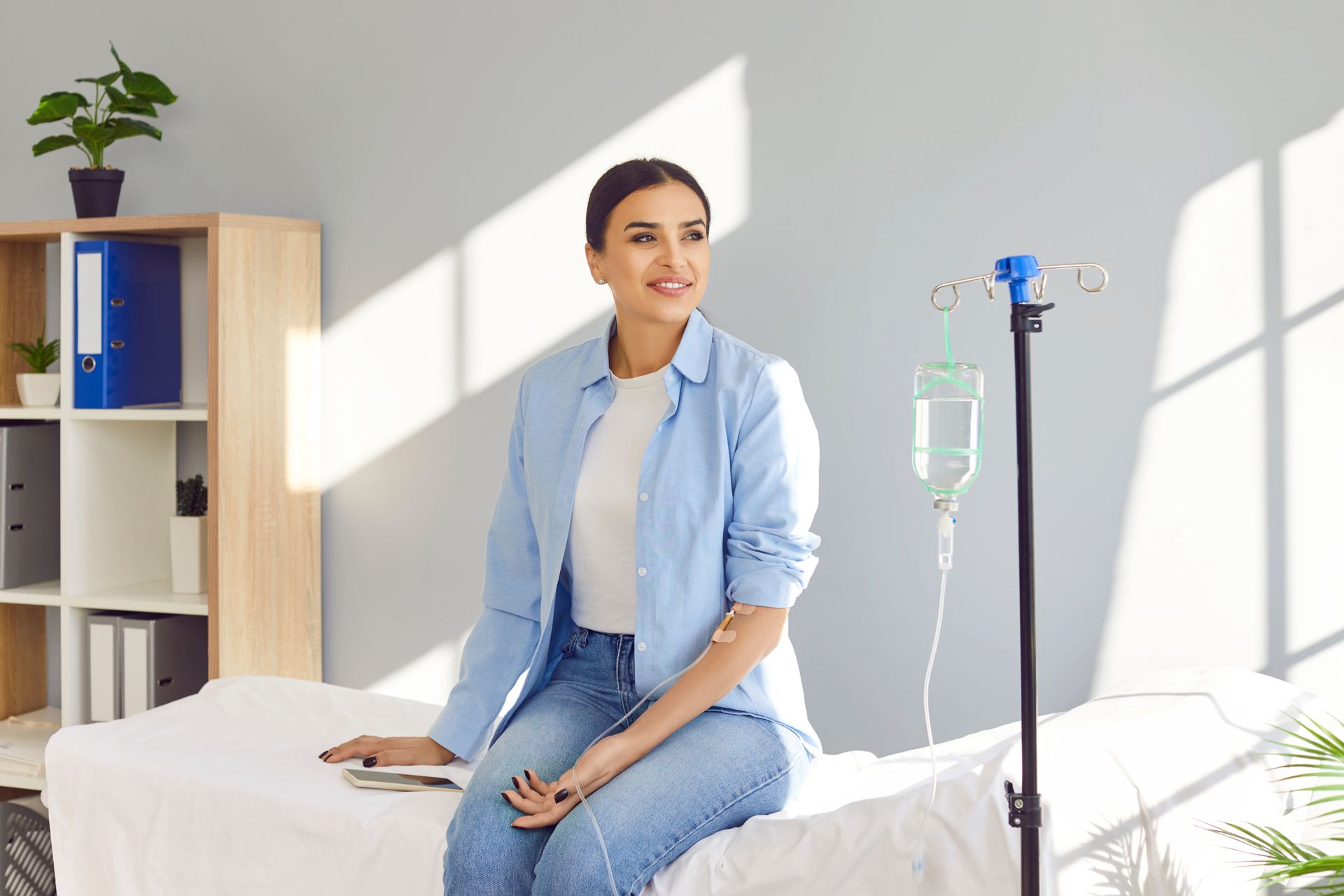 Patient sitting on a hospital bed beside an IV stand in a bright, clean room