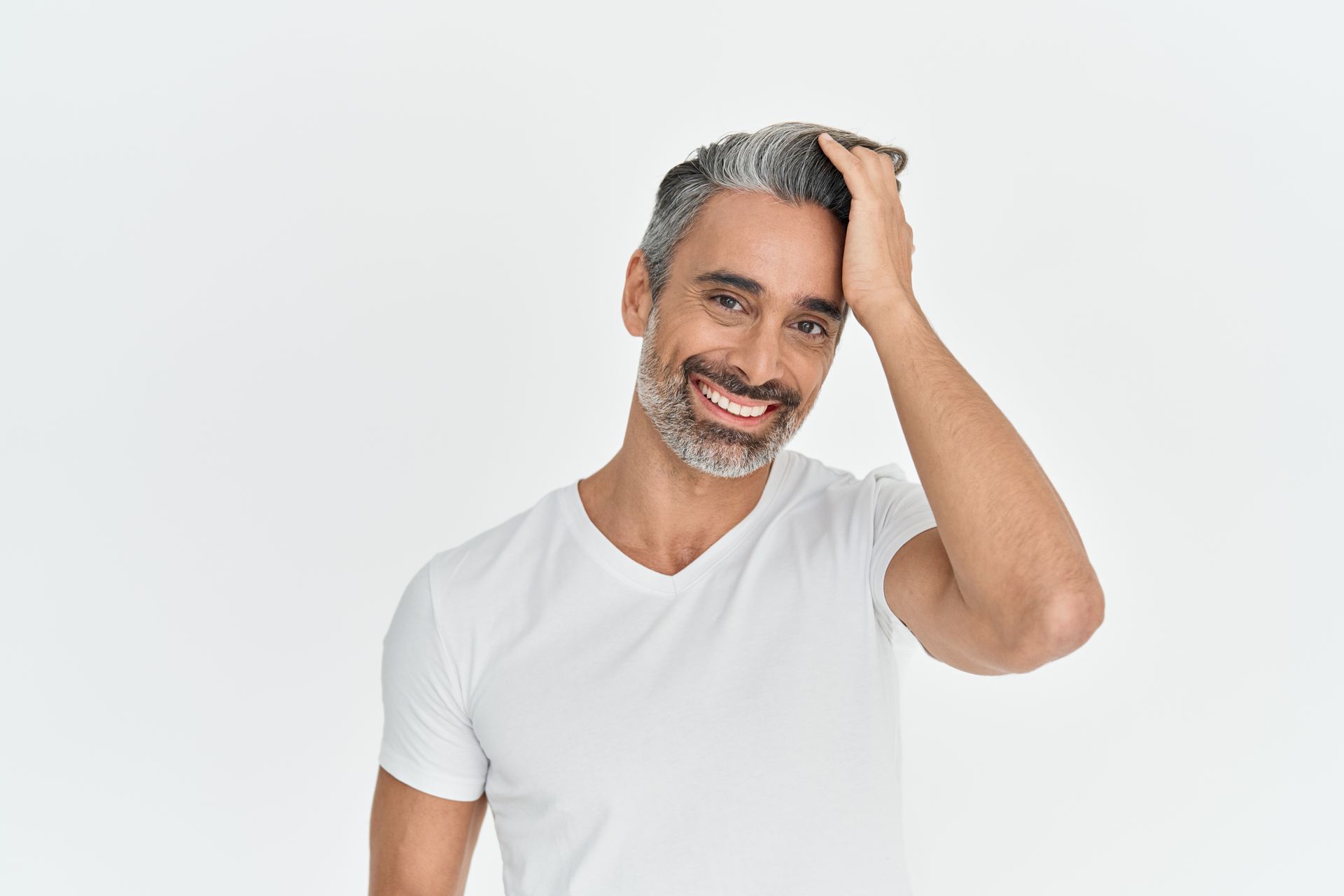 Smiling person in a white T-shirt touching their hair against a light gray background