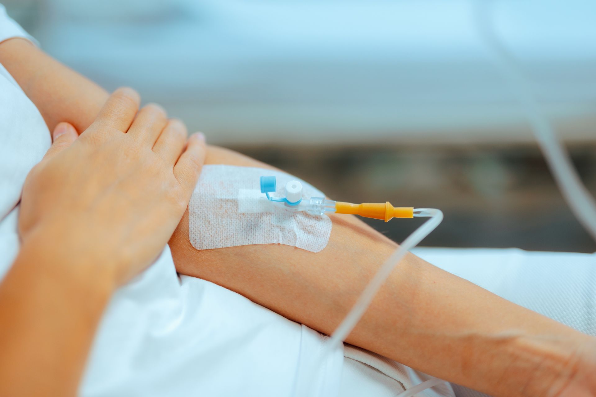 Close-up of a patient’s arm with an IV catheter and taped infusion line in a hospital setting