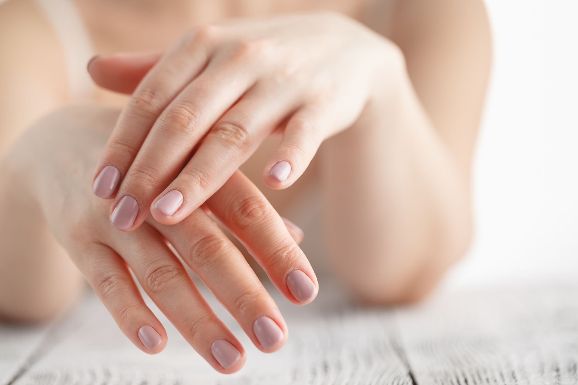 Hands with pale pink nails resting on a white surface
