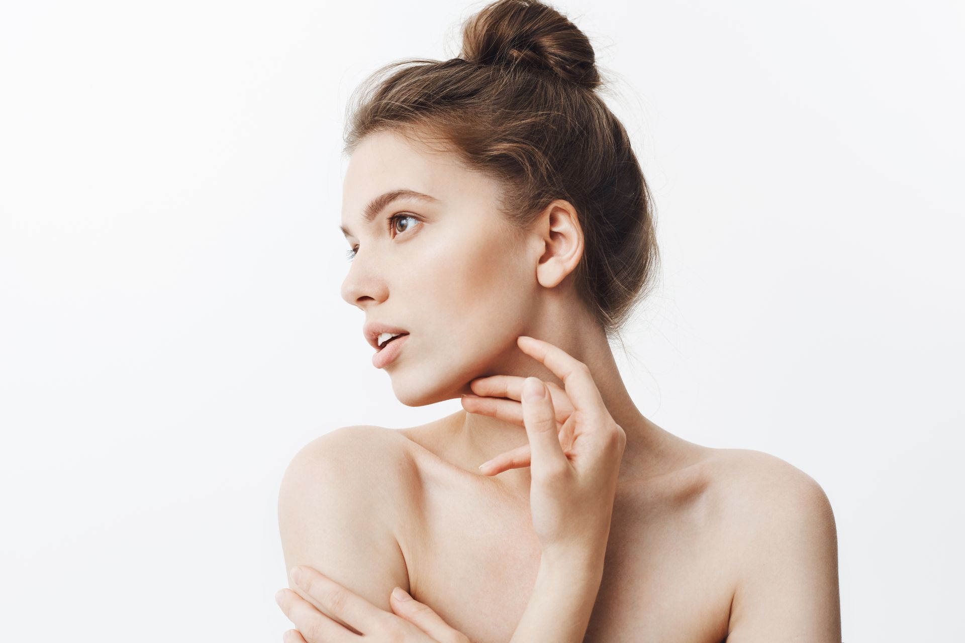 Portrait of a woman with hair in a bun, touching her neck against a white background