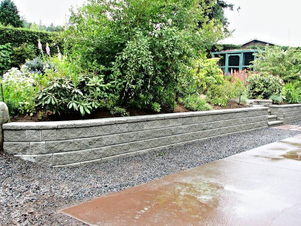 Concrete block retaining wall supports raised garden bed beside gravel path in backyard
