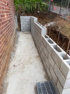 Construction site with concrete block wall along a narrow walkway beside a brick building