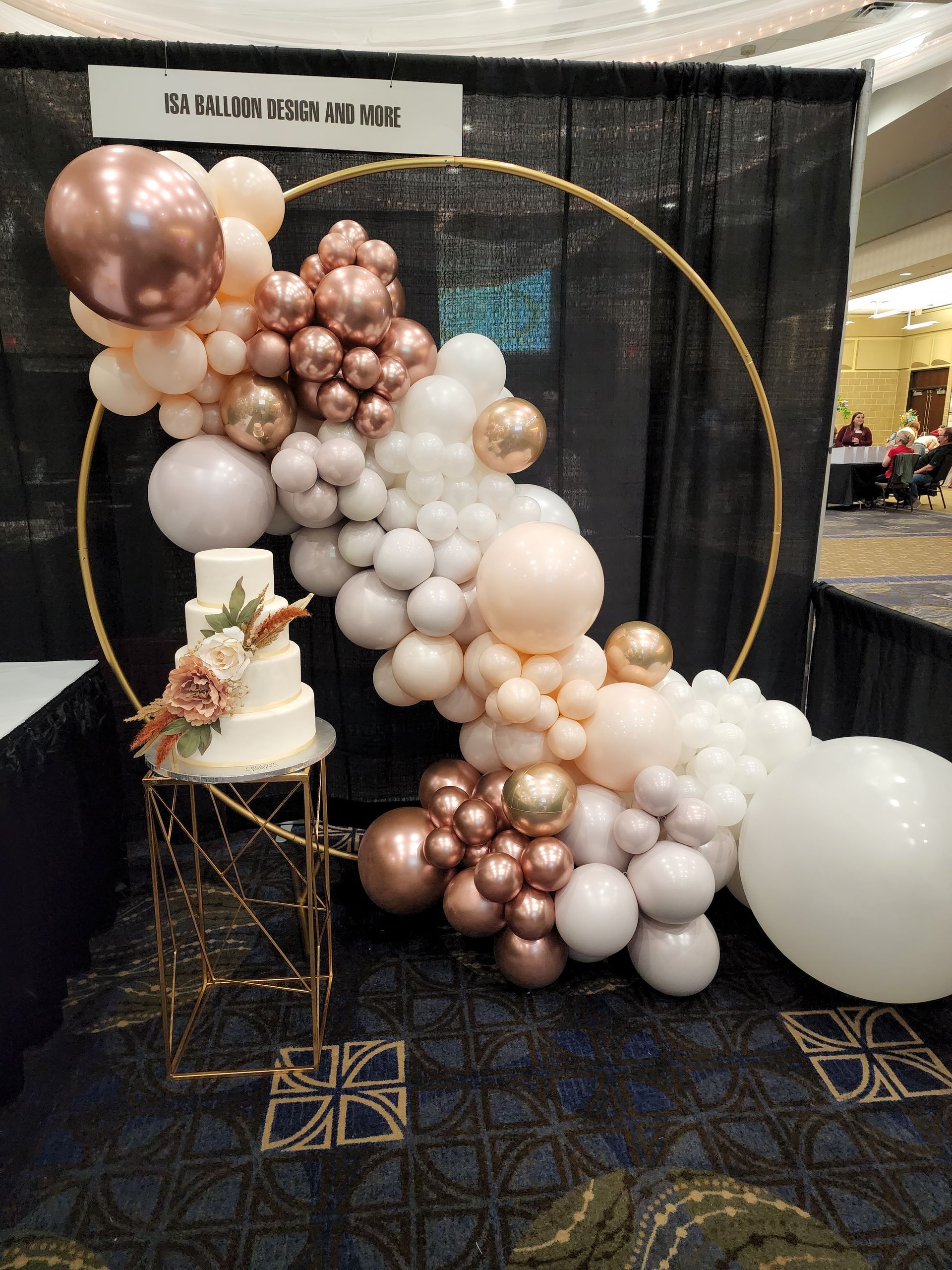 A wedding cake is sitting on a table in front of a balloon arch.
