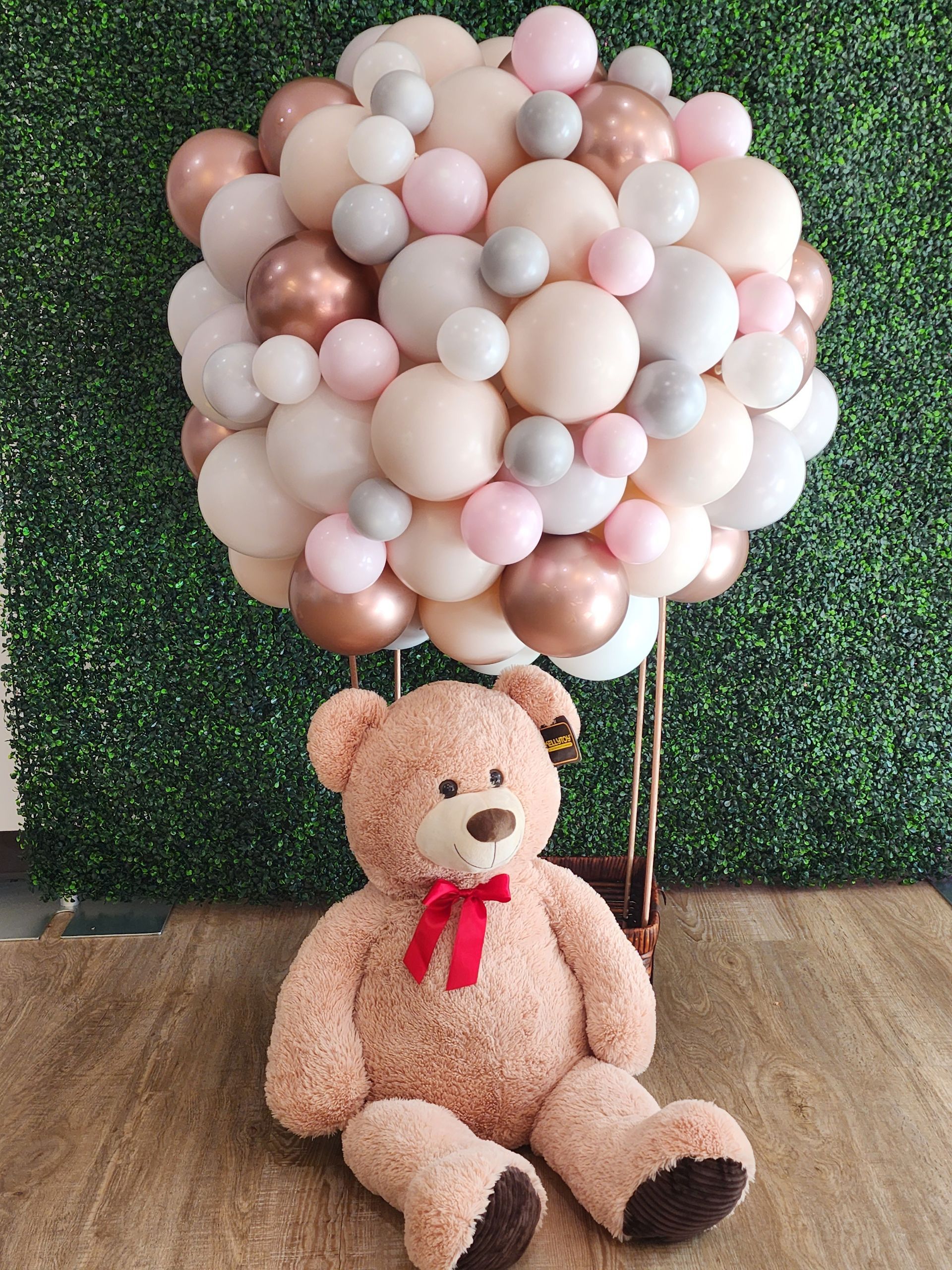A teddy bear is sitting under a hot air balloon made of balloons.