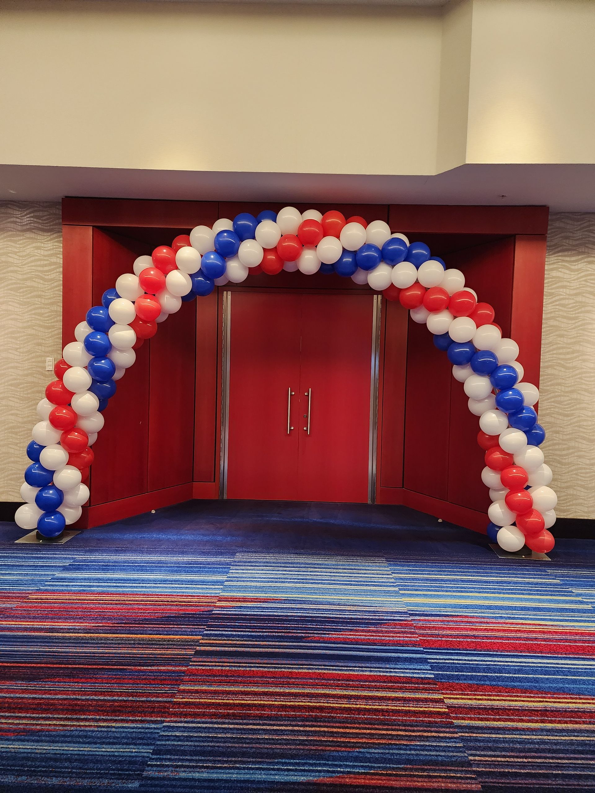A red , white , and blue balloon arch in a room.